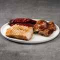 Plated dish with sliced pork belly, BBQ pork, and roasted duck on a gray background