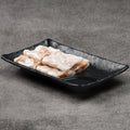 Rice noodle rolls on a black rectangular plate against a gray background