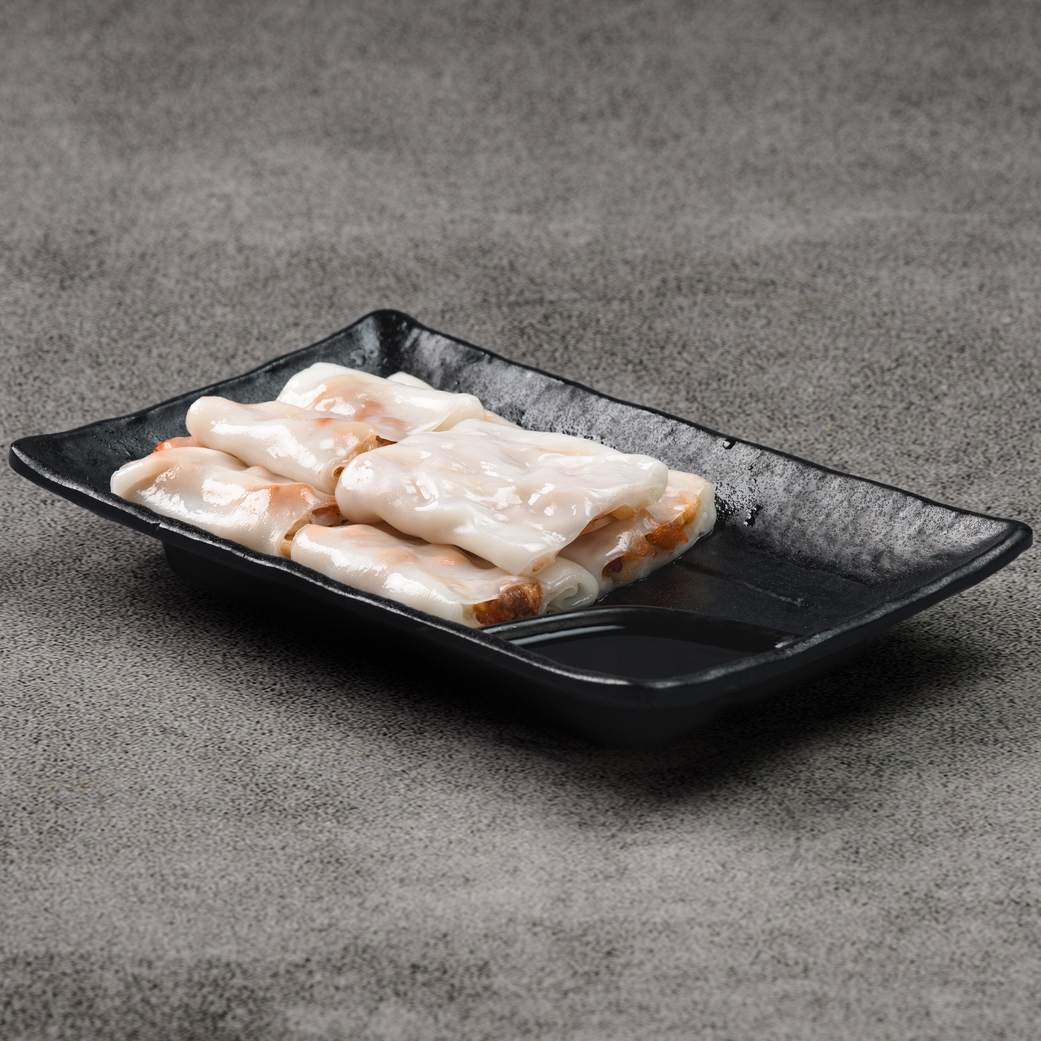 Rice noodle rolls on a black rectangular plate against a gray background