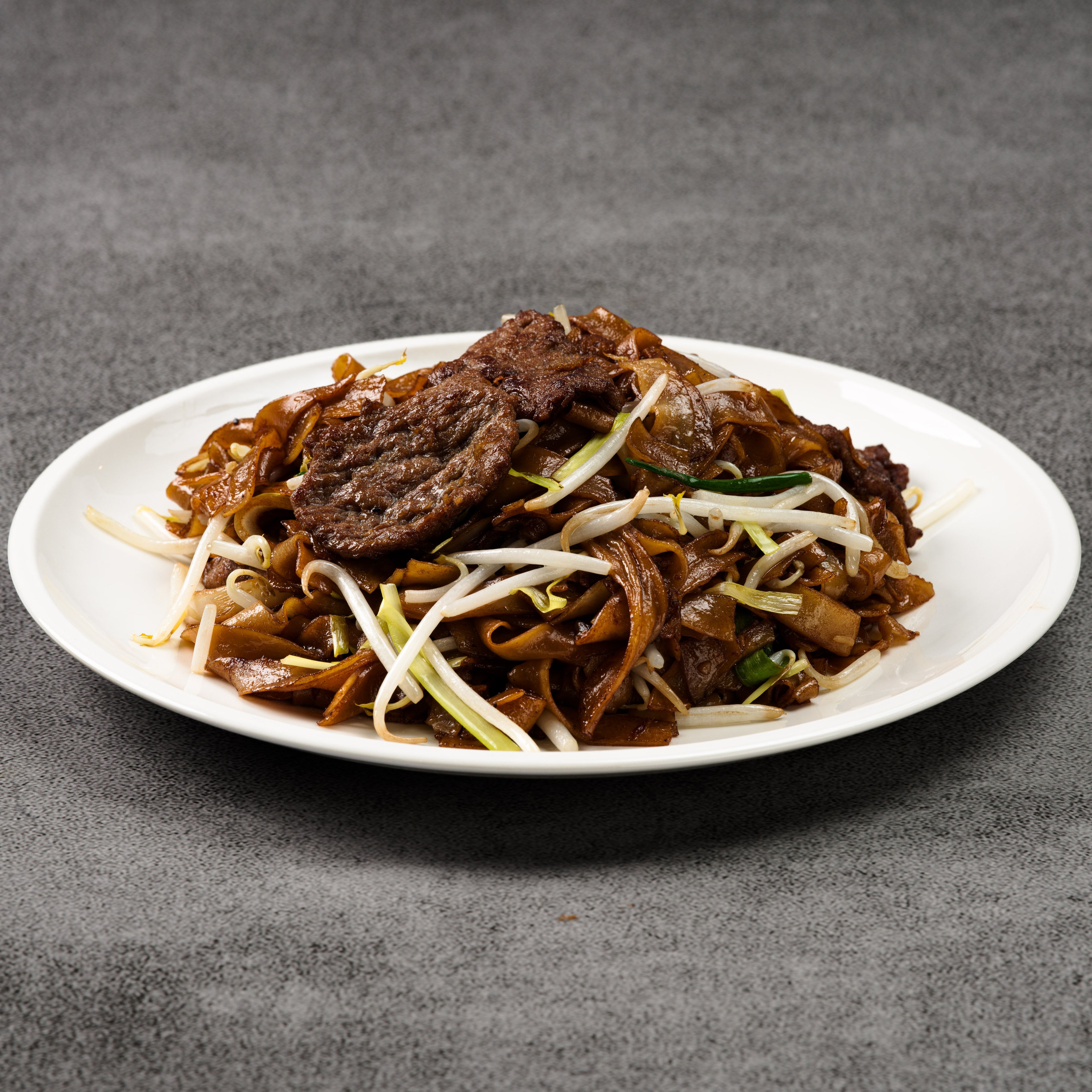 Plated dish of noodles with meat and vegetables on a gray background