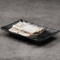 Rice noodle rolls on a black rectangular plate against a gray background