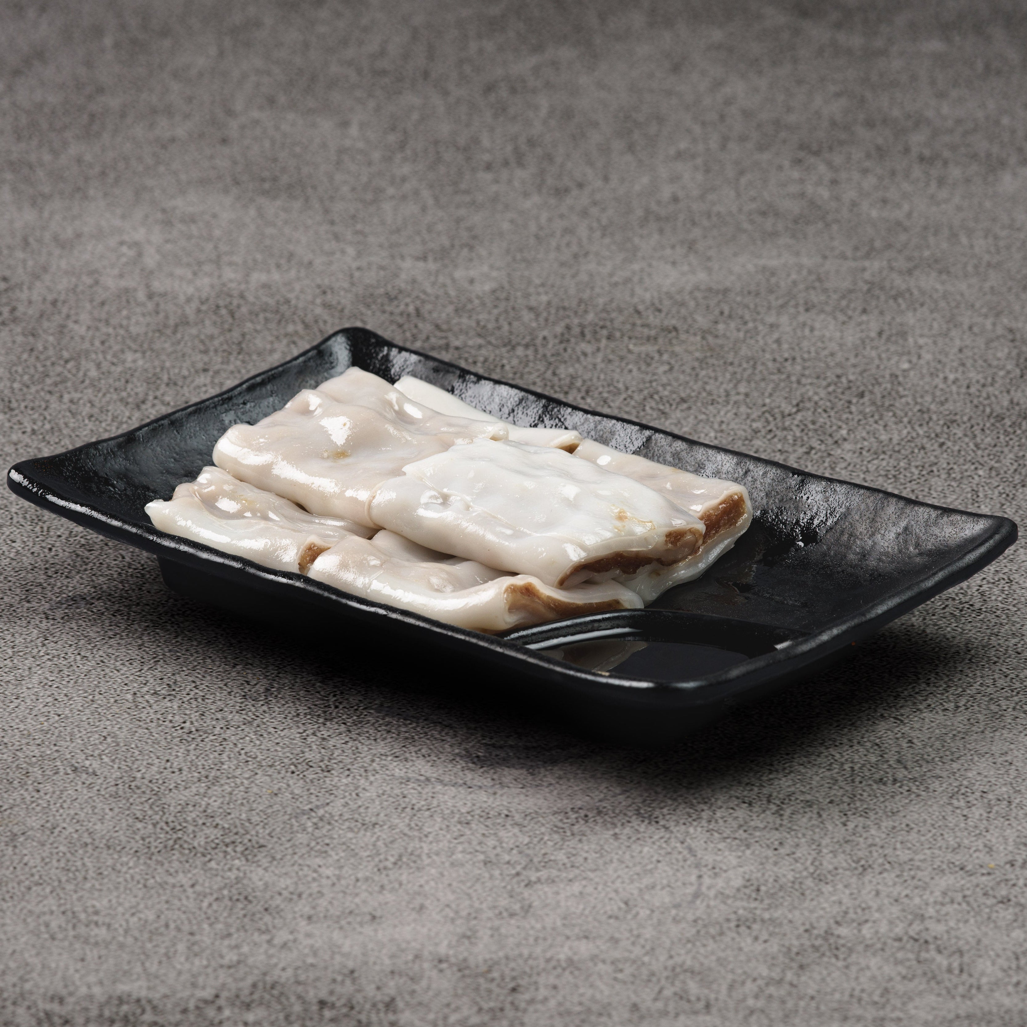Rice noodle rolls on a black rectangular plate against a gray background