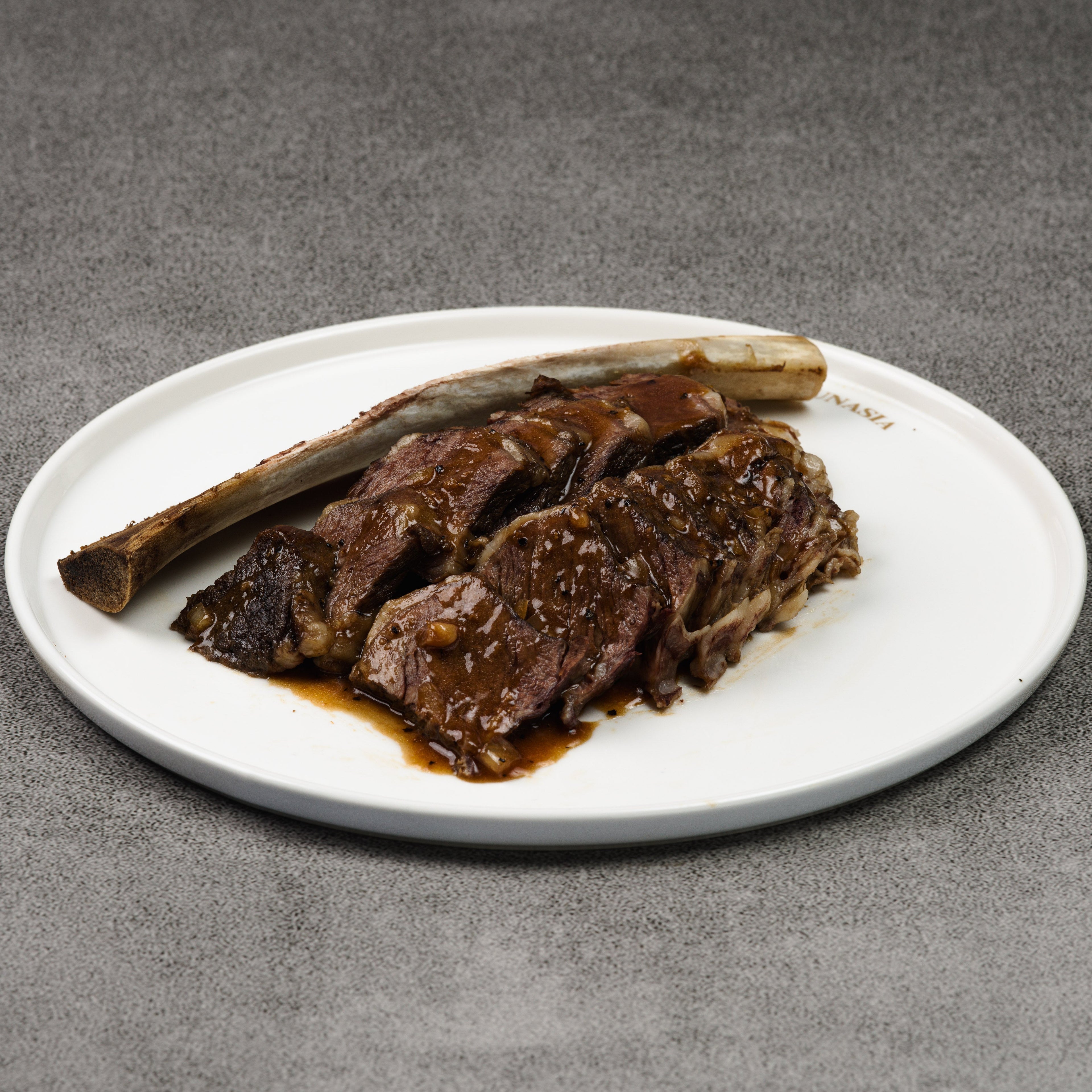 Sliced beef with a bone on a white plate against a gray background