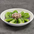 White bowl with green vegetables and minced taro on a gray background