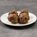 Three meatballs on a white plate against a gray background