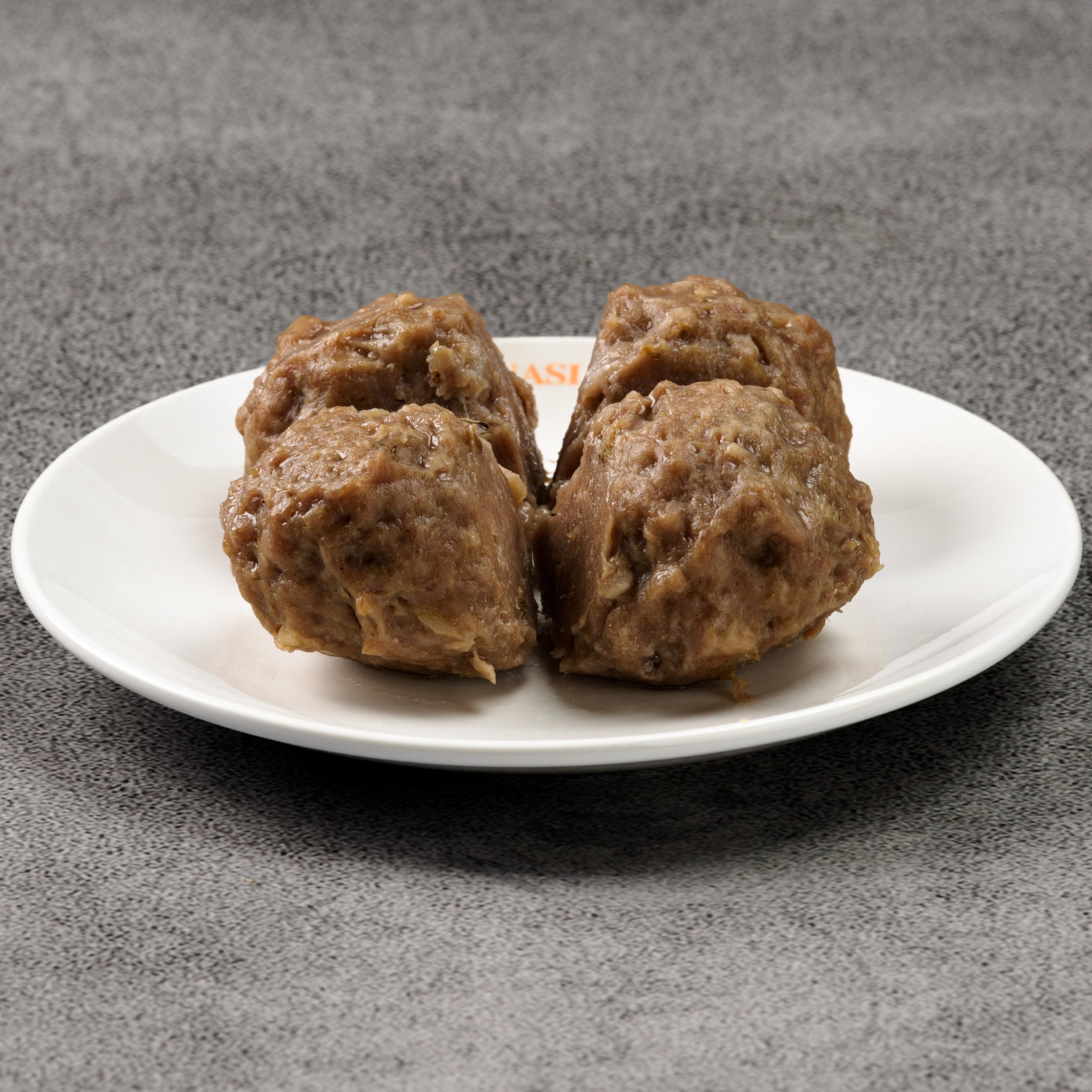 Three meatballs on a white plate against a gray background