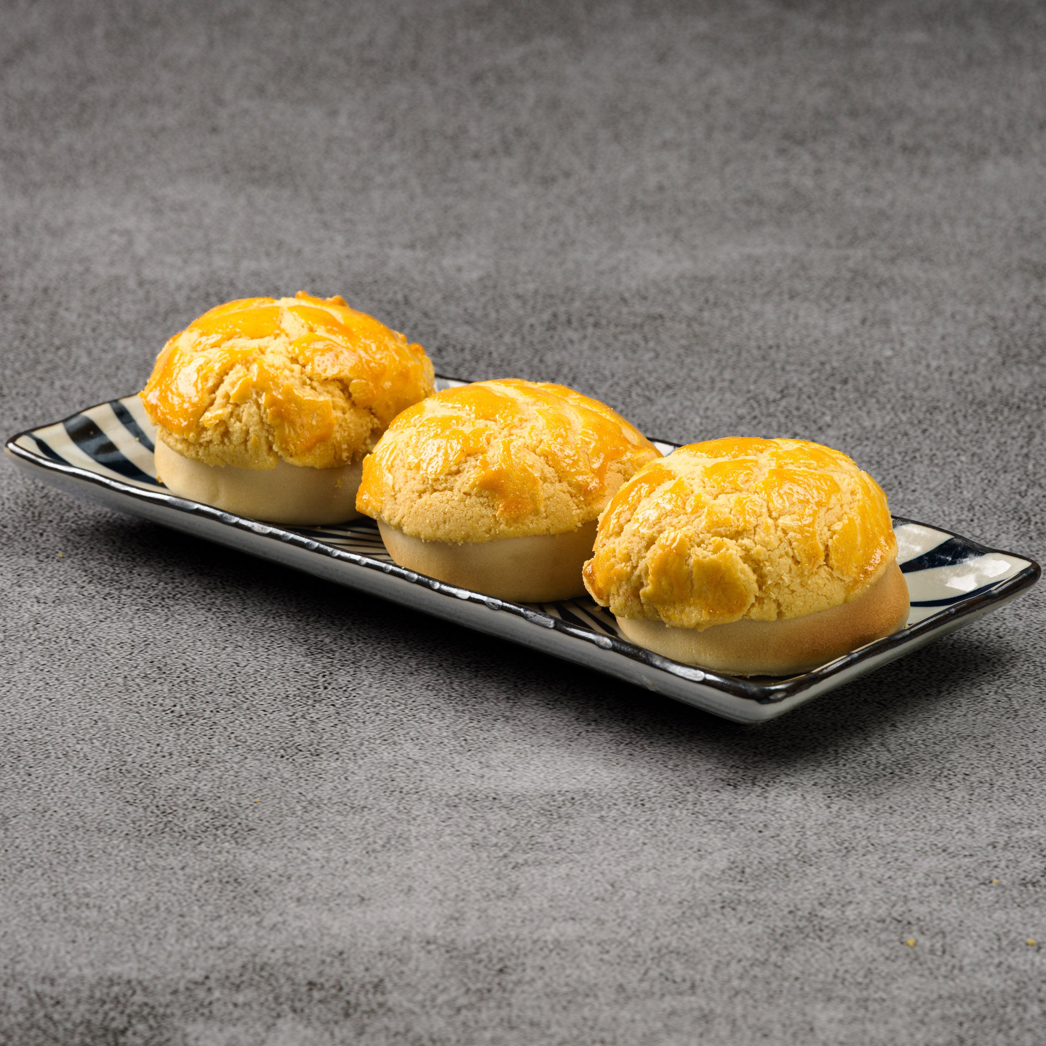 Three pastries on a rectangular black plate with a striped pattern against a gray background