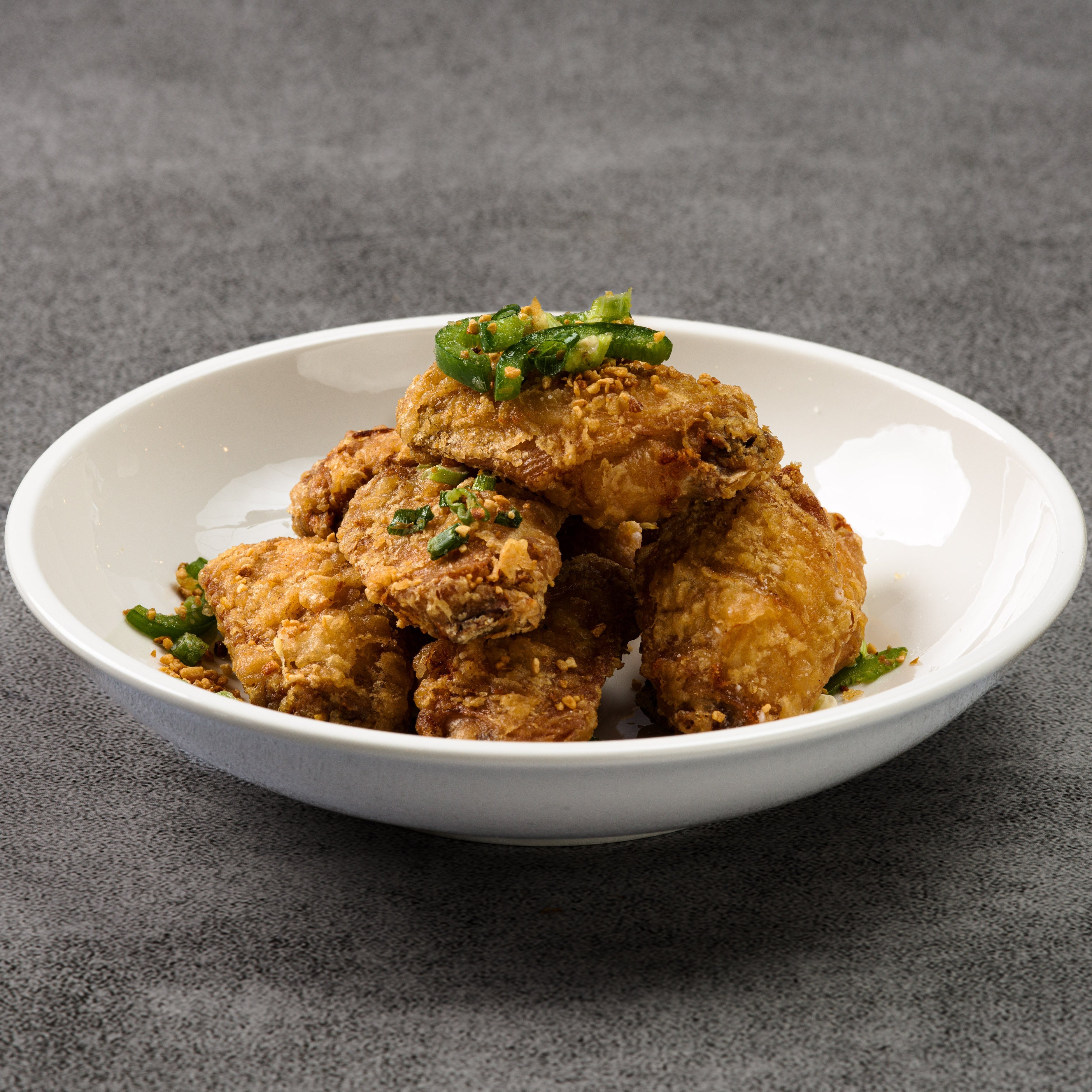 Fried chicken with green onions on a white plate against a gray background