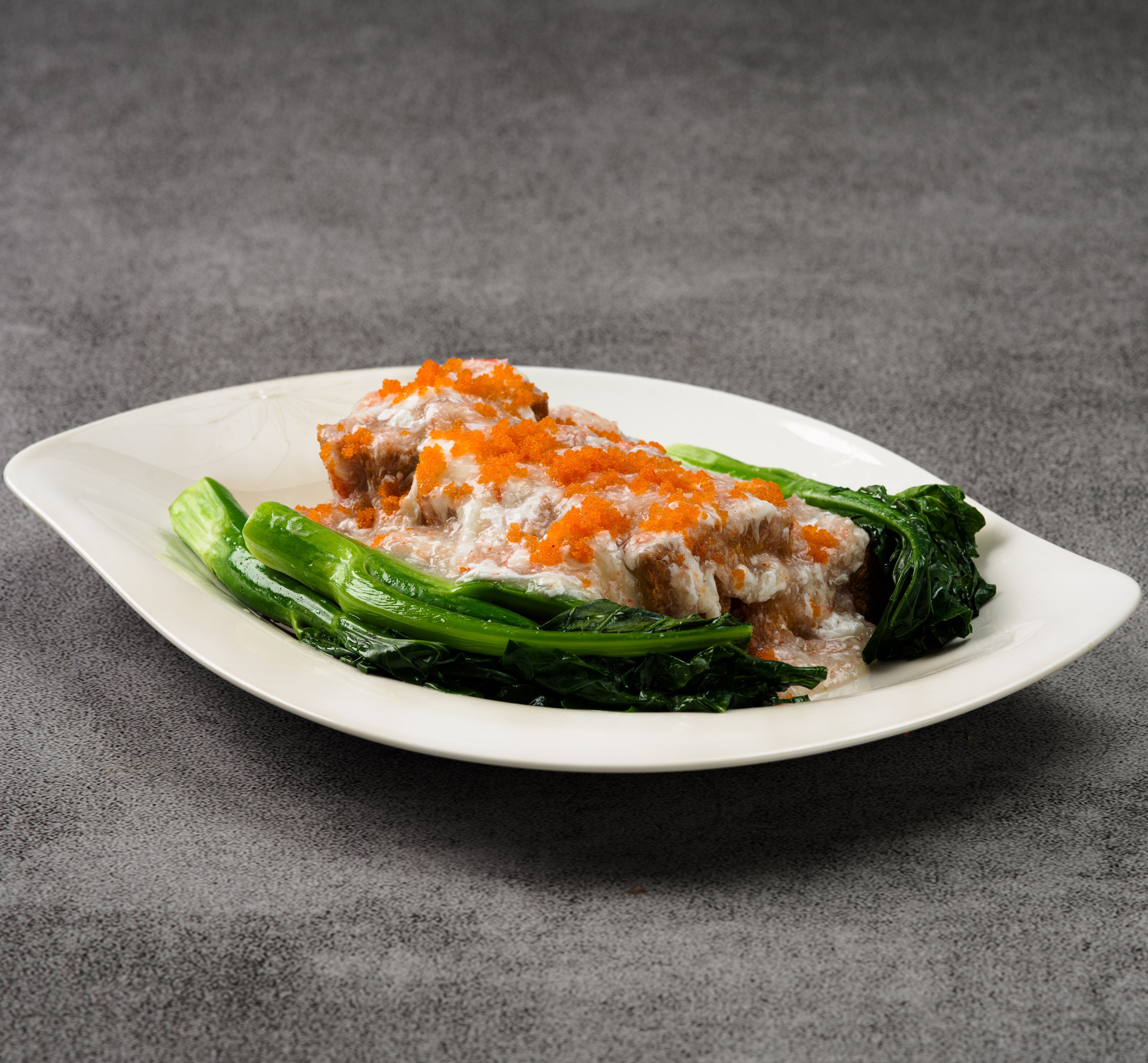 Plated dish with tofu and crab and vegetables on a gray background