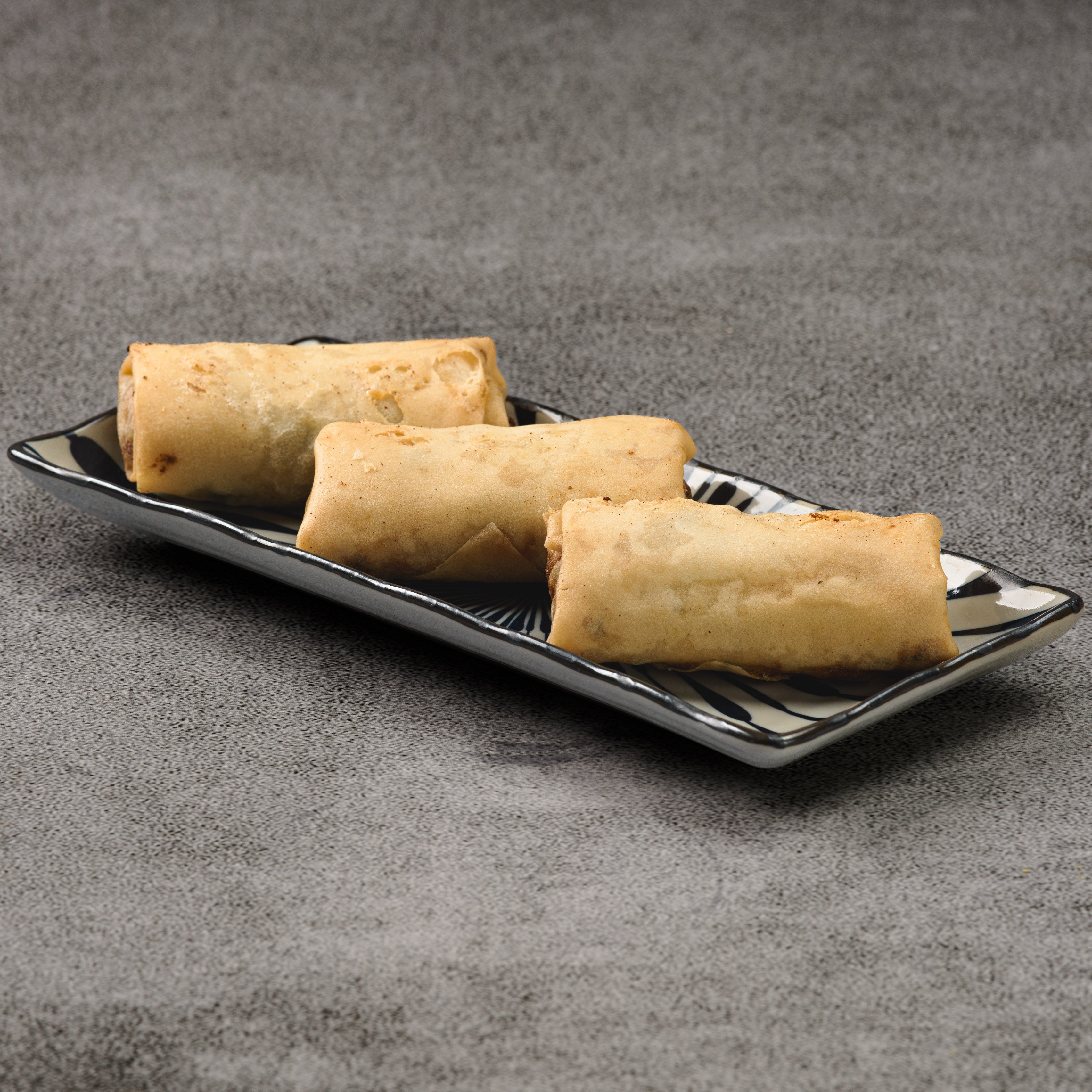 Three spring rolls on a black rectangular plate against a gray background