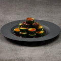 Cucumber slices with sauce on a black plate against a gray background