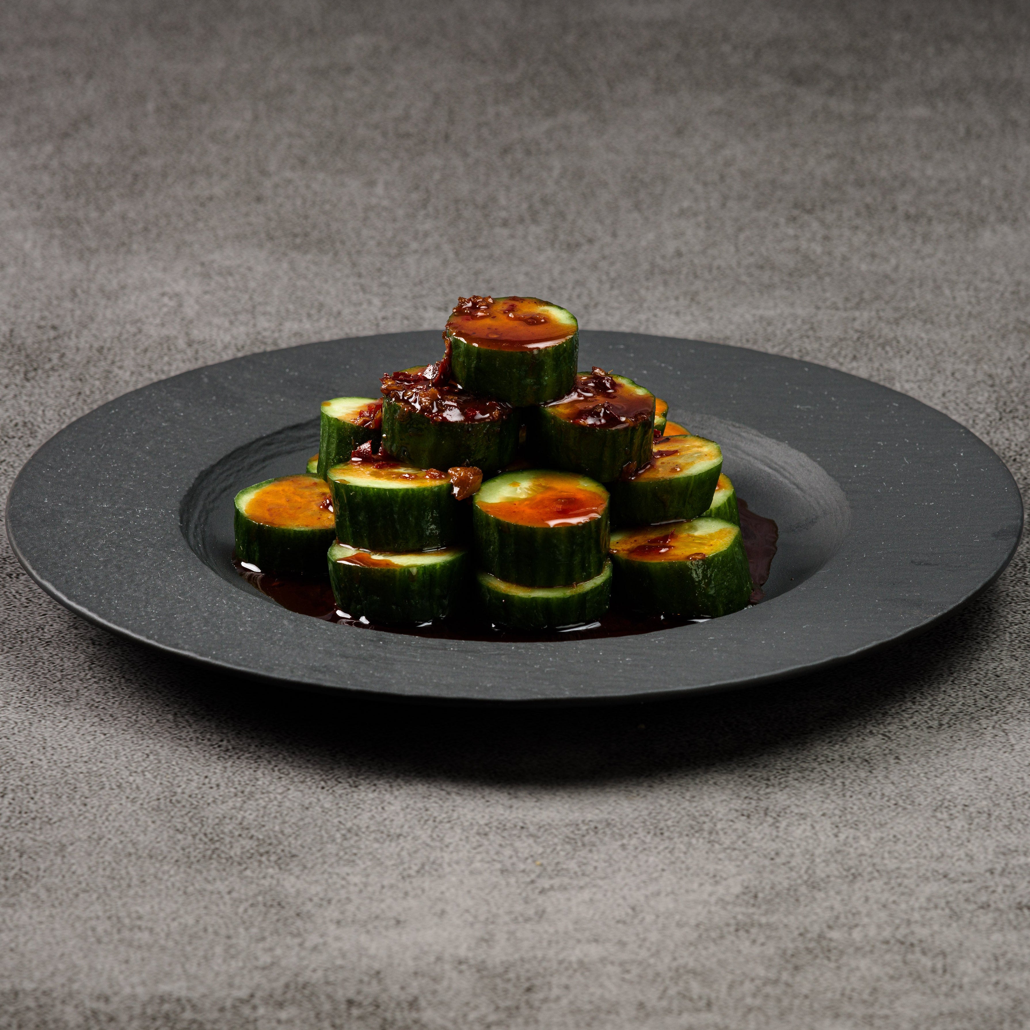 Cucumber slices with sauce on a black plate against a gray background