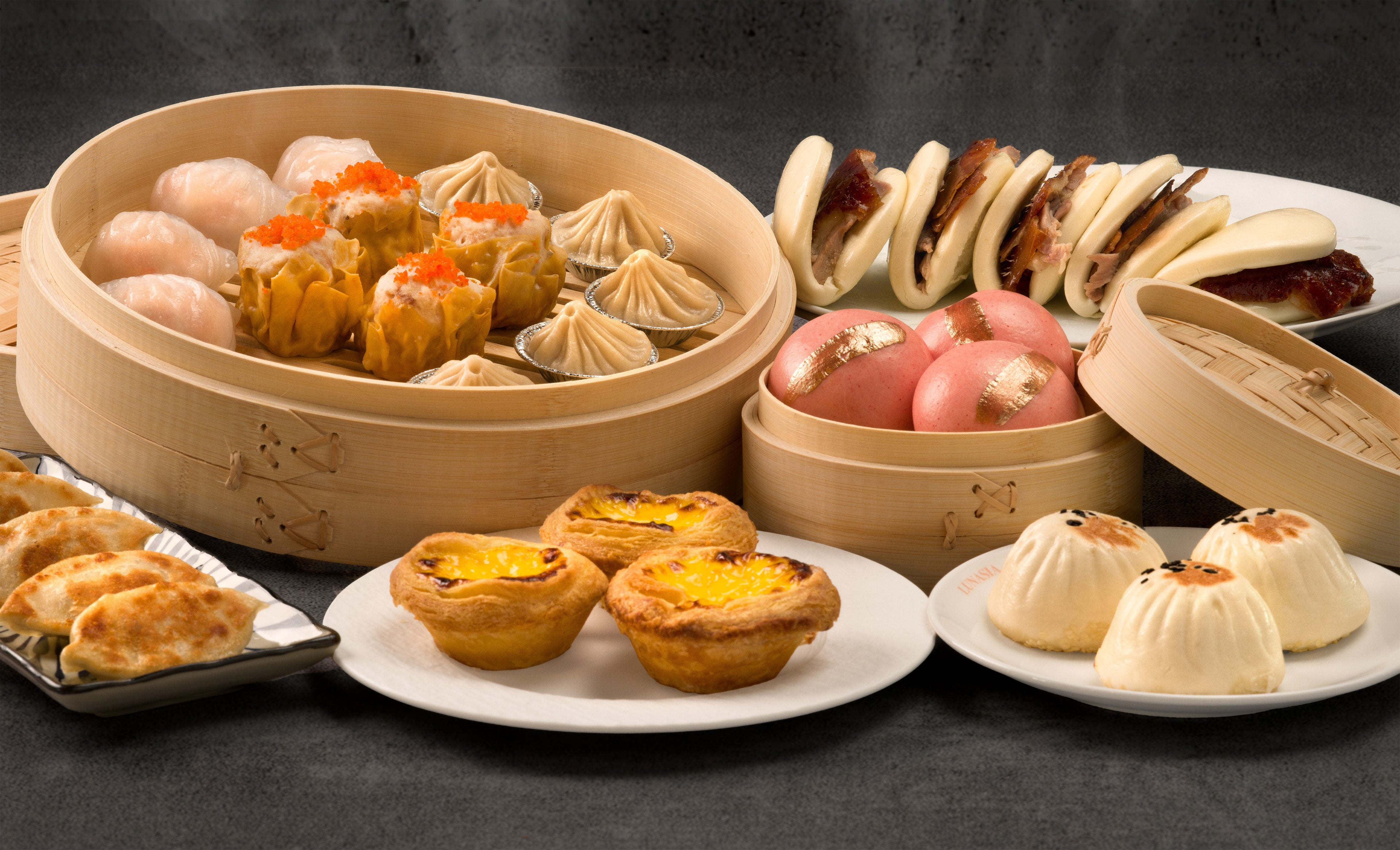 Assorted Chinese dim sum including baozi, siu mai, and other pastries on a dark background.