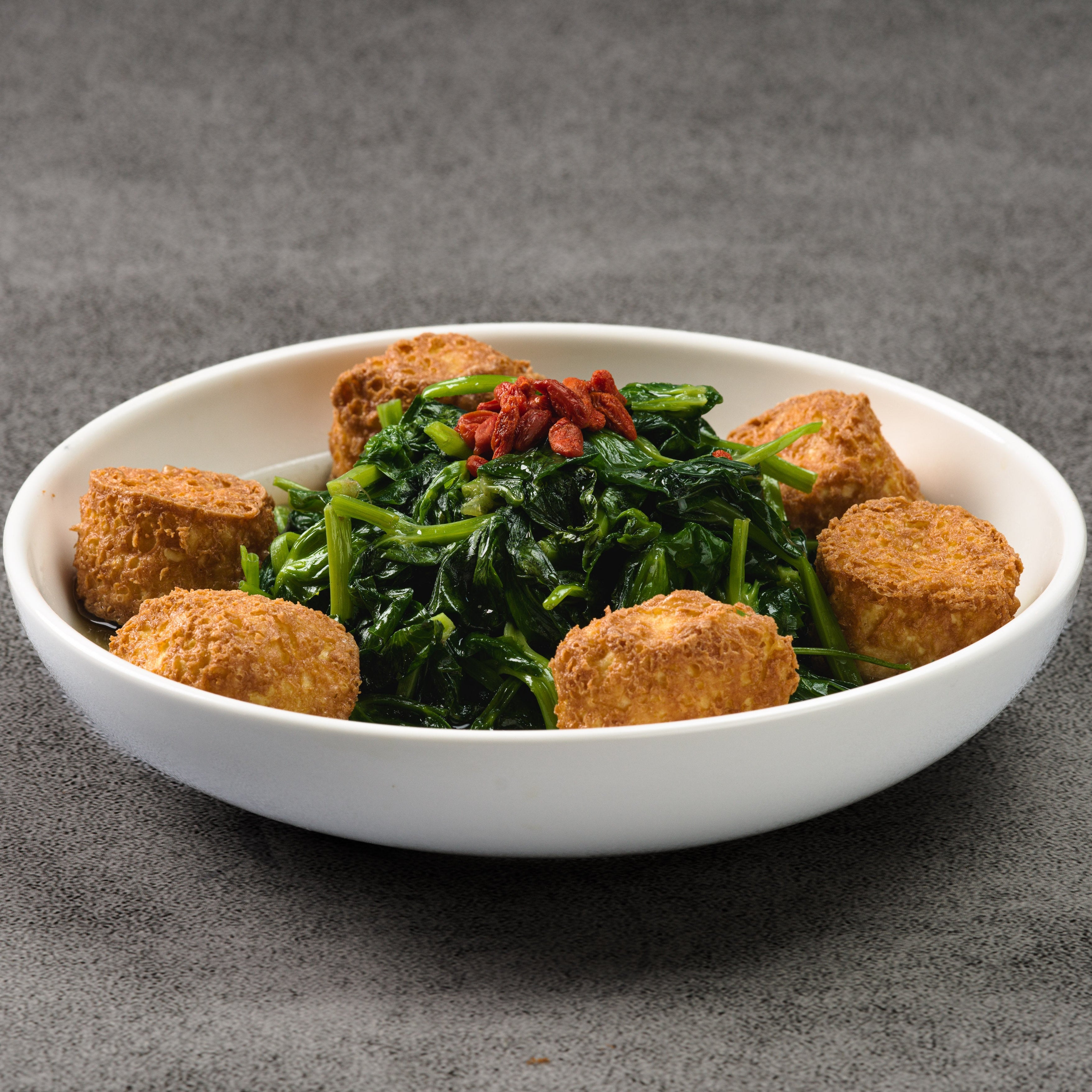 White bowl with green leafy vegetables and fried tofu on a gray background