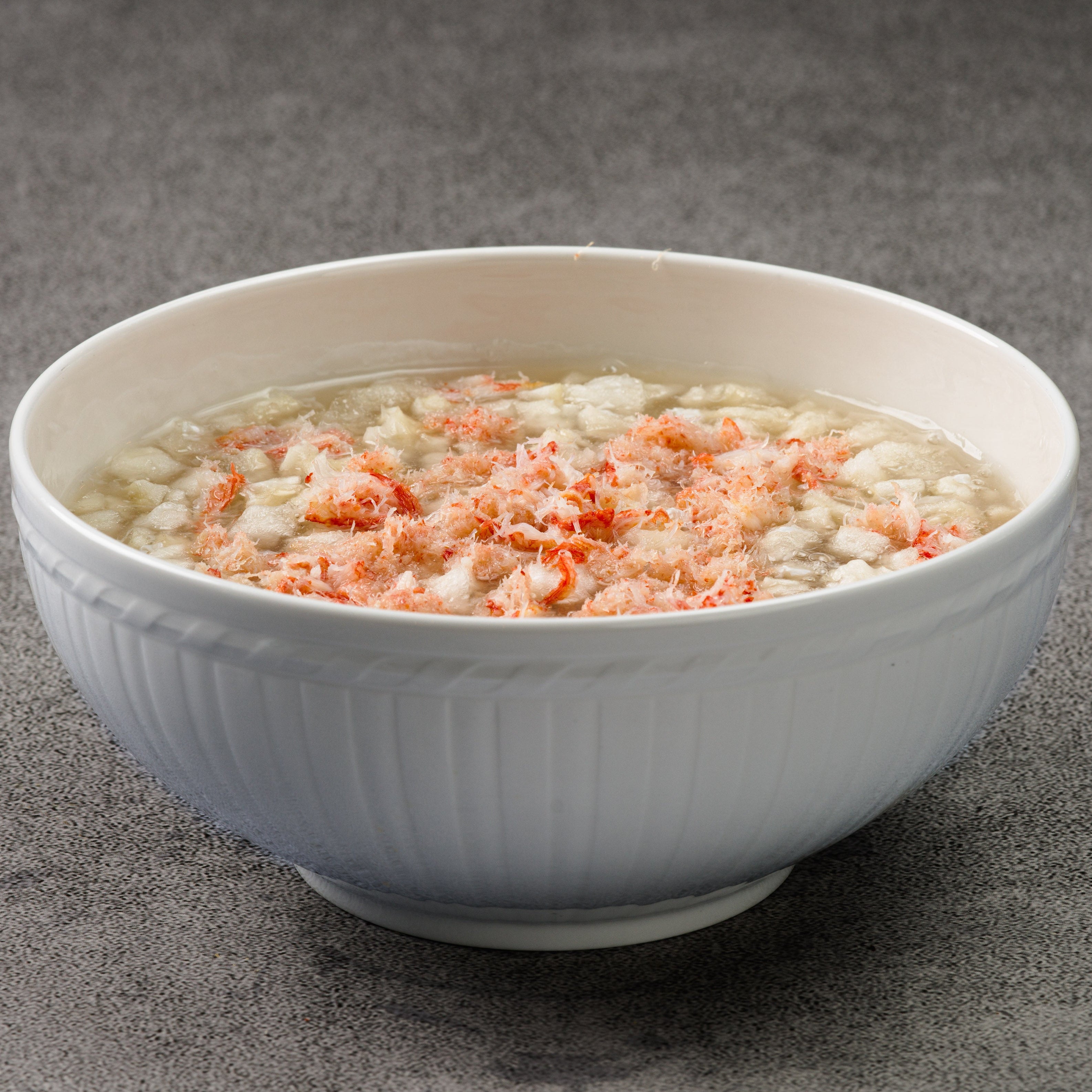 White bowl of soup with fish and crab on a gray background
