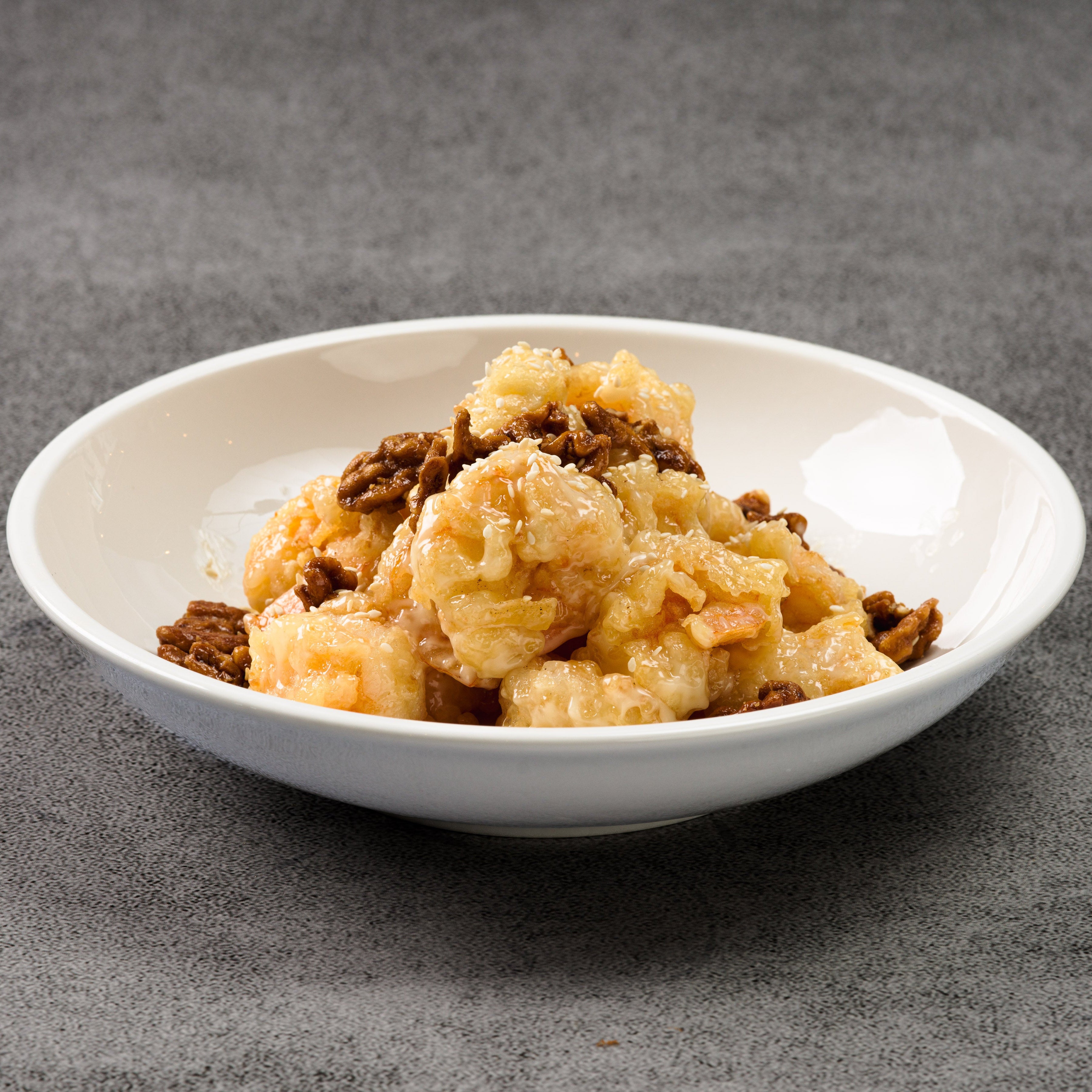 White bowl with honey walnut shrimp on a gray background