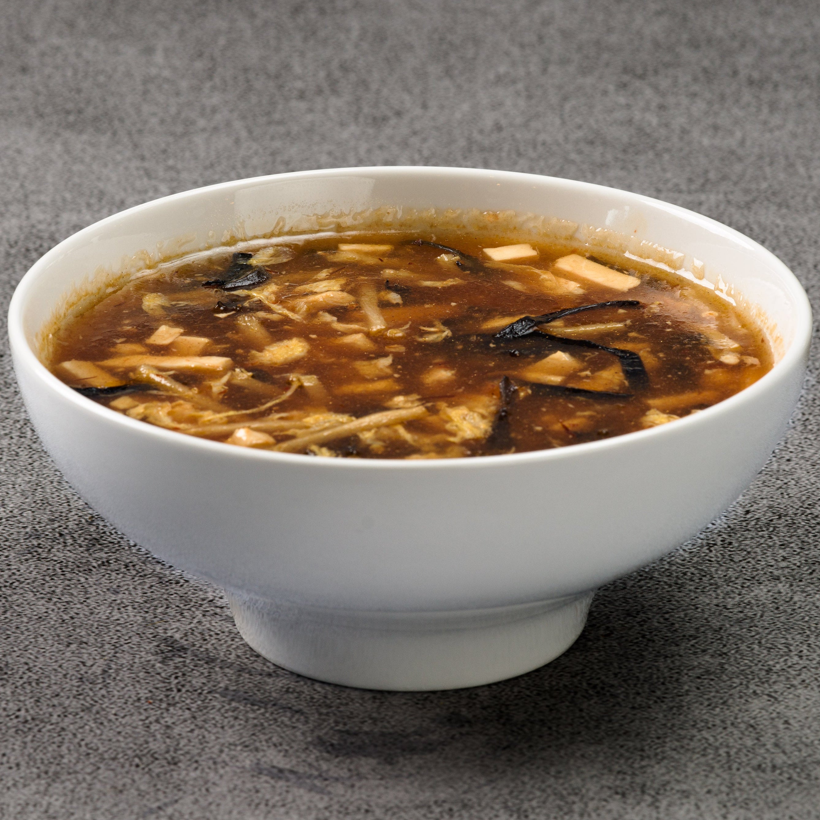 White bowl of hot and sour soup on a gray background