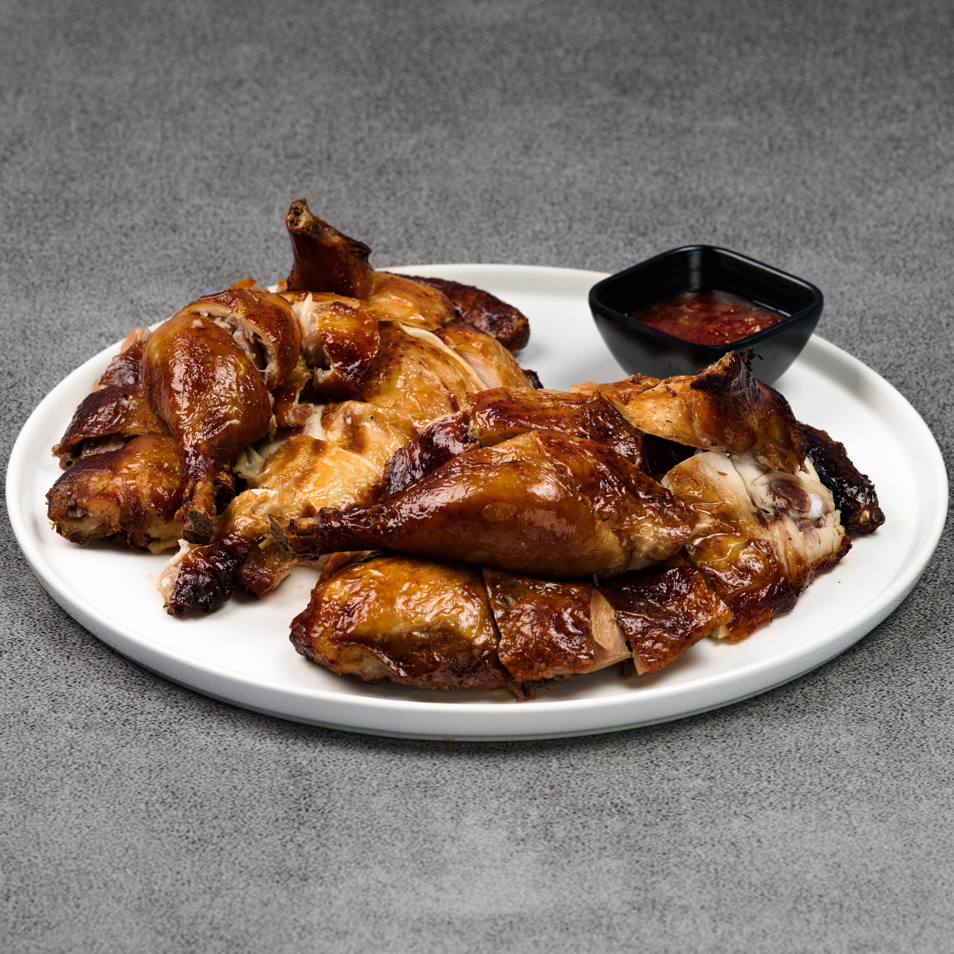 Plated roasted chicken with a side of dipping sauce on a gray background