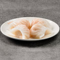 Four shrimp dumplings on a white plate against a gray background