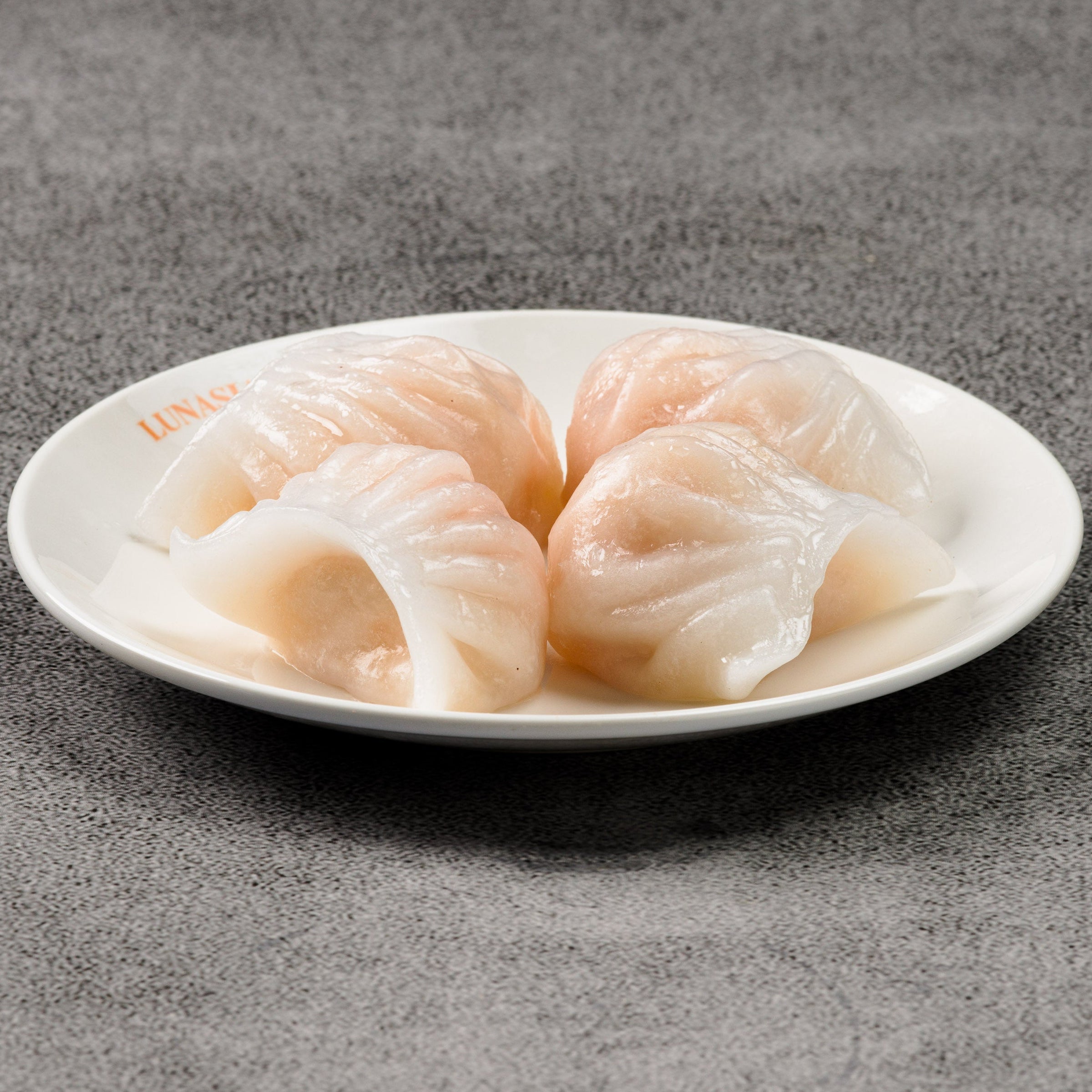 Four shrimp dumplings on a white plate against a gray background