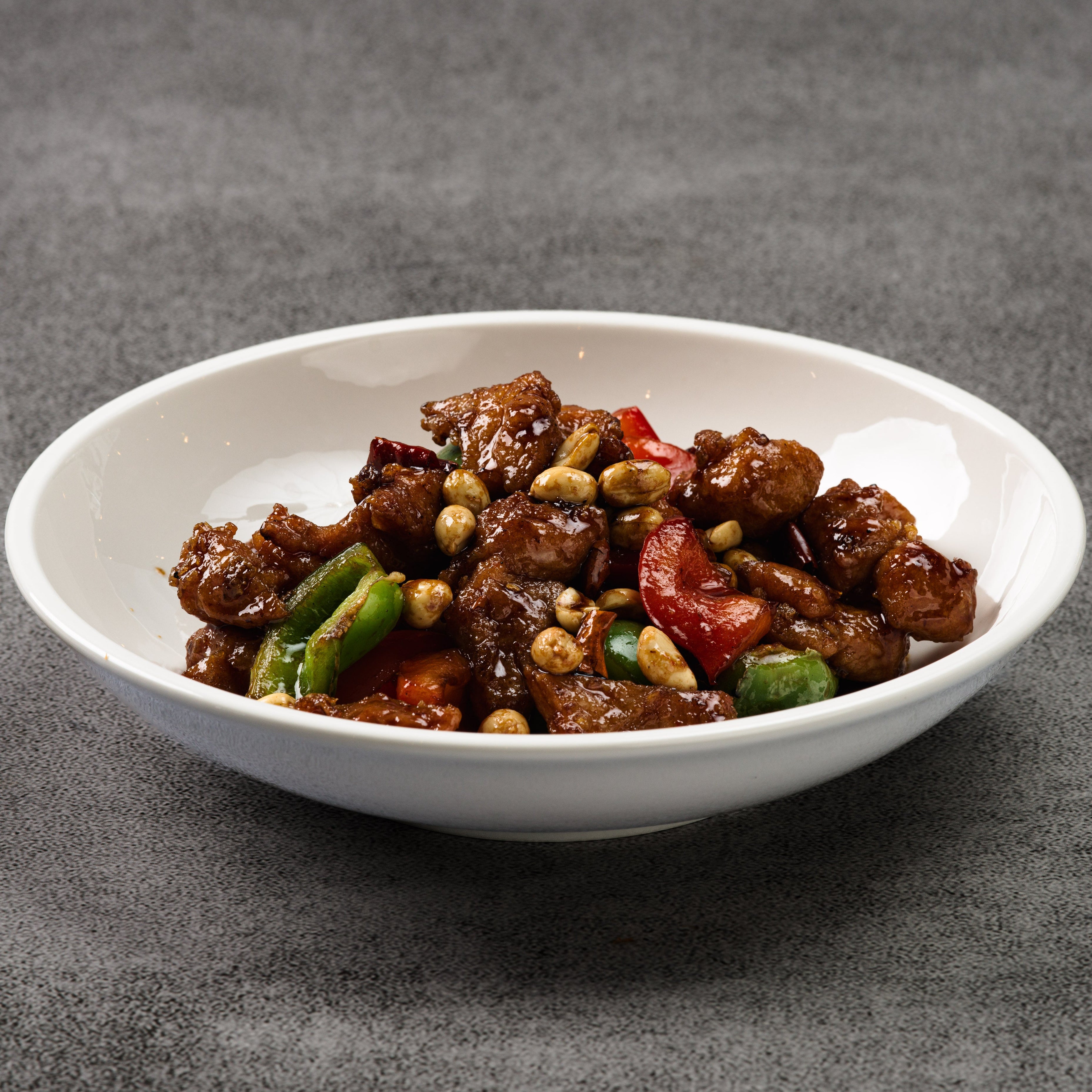 White bowl filled with a chicken stir-fry dish on a gray background