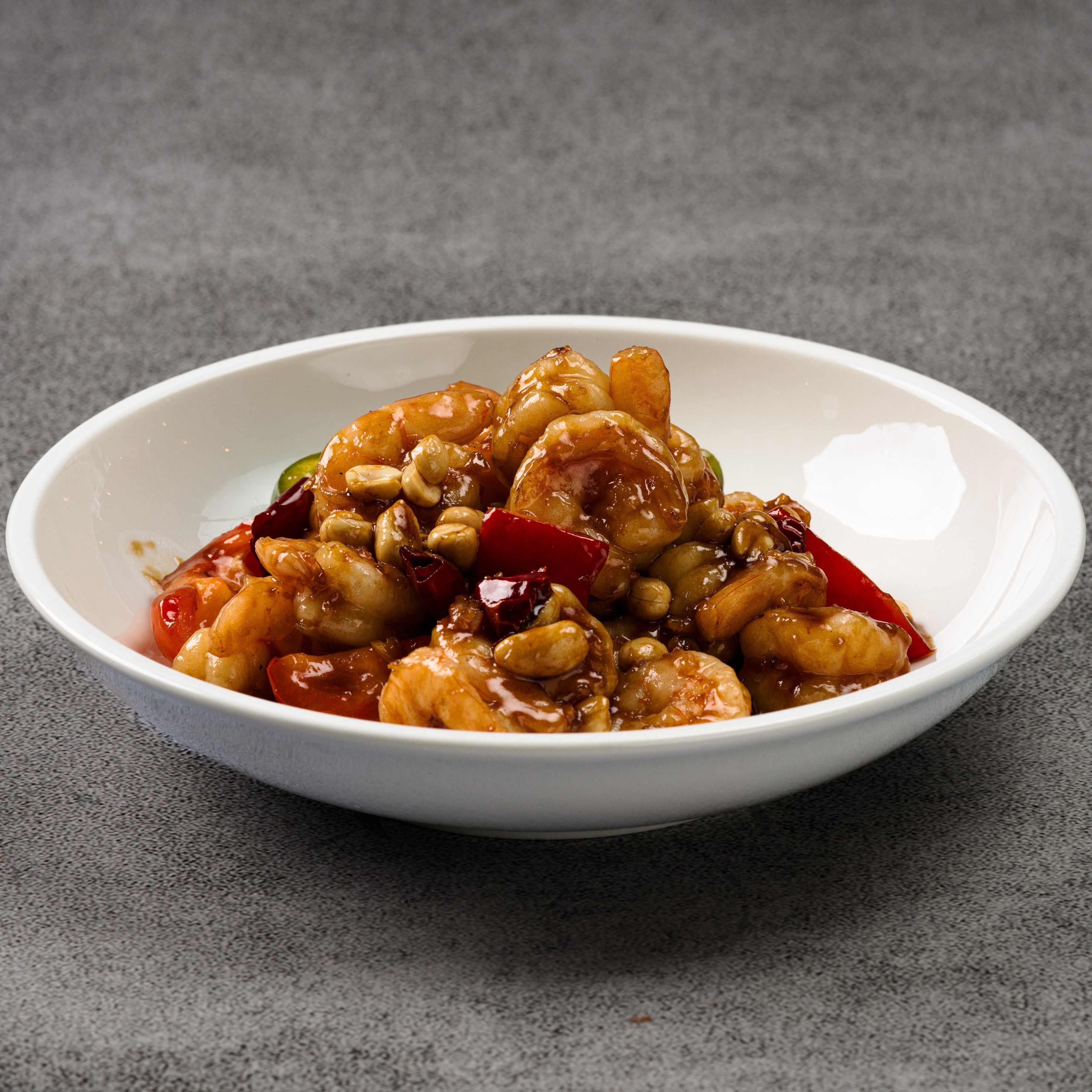 White bowl of spicy shrimp and vegetables dish on a gray background