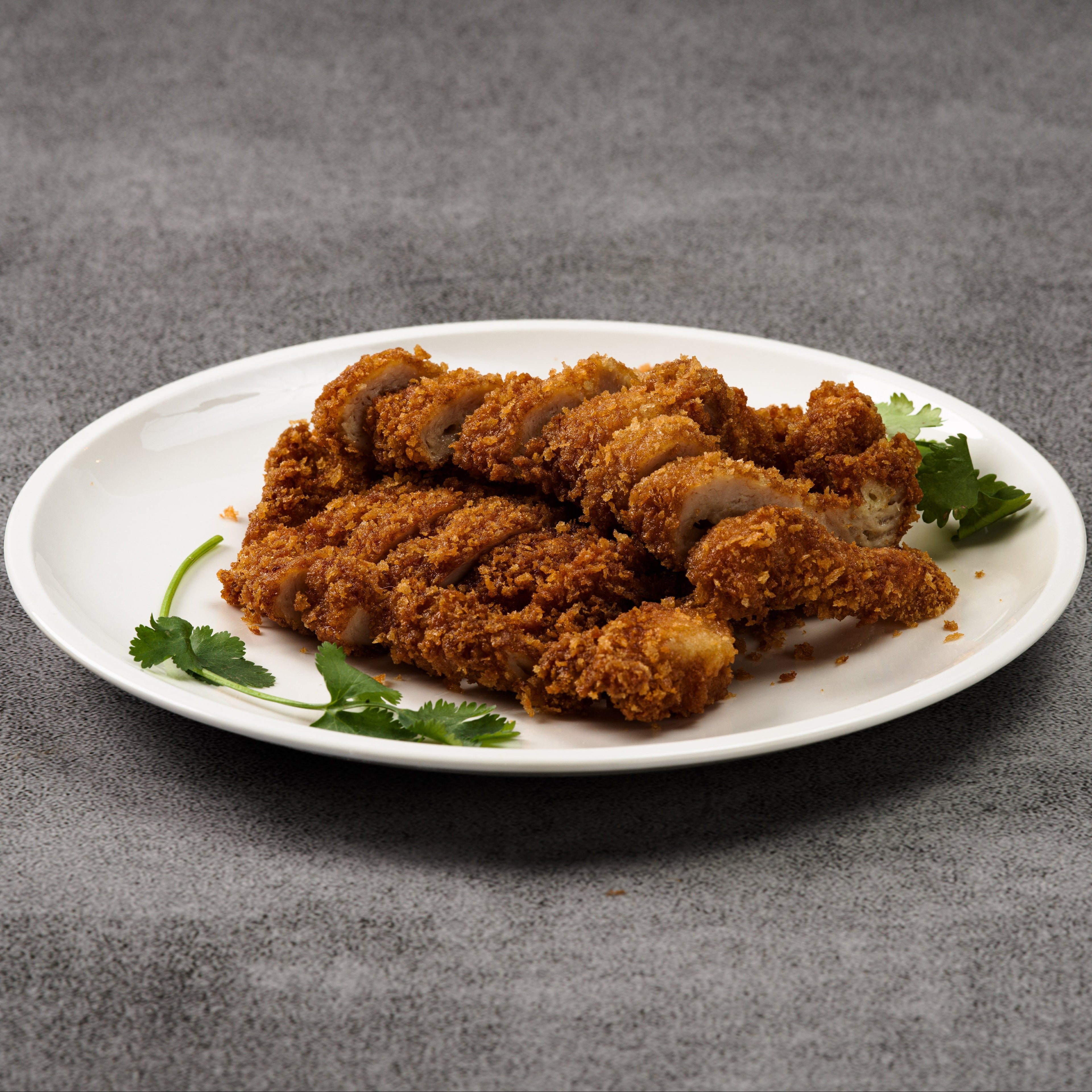 Fried pork on a white plate with green herbs on a gray background