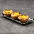 Three egg tarts on a rectangular plate with a gray background