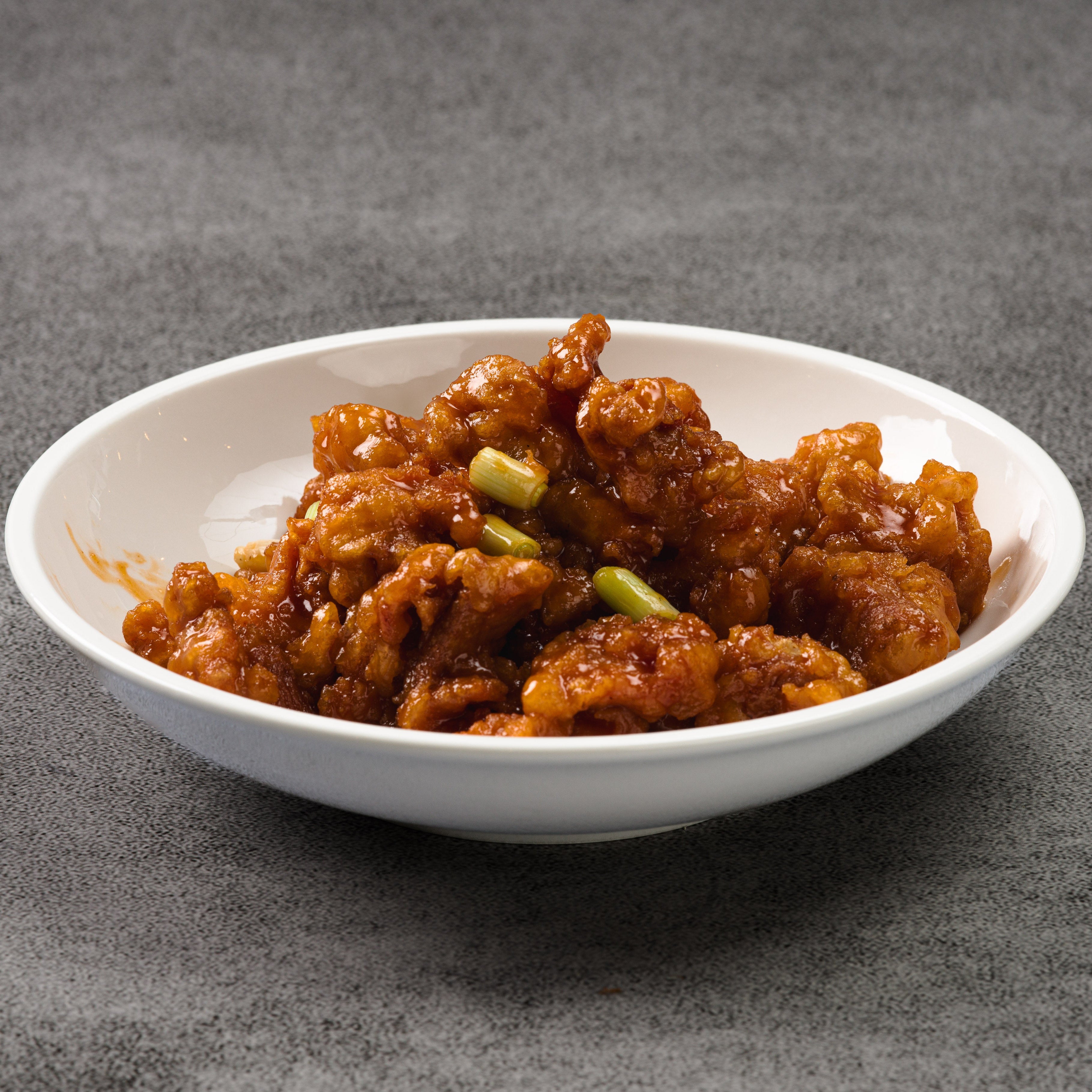 White bowl with orange chicken on a gray background