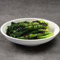 Bowl of green leafy vegetables with a dark sauce on a gray background