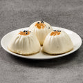 Three white dumplings on a white plate against a gray background