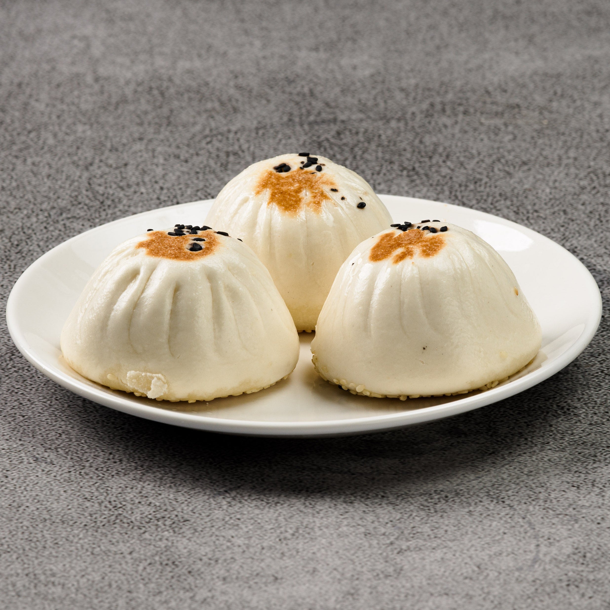 Three white dumplings on a white plate against a gray background