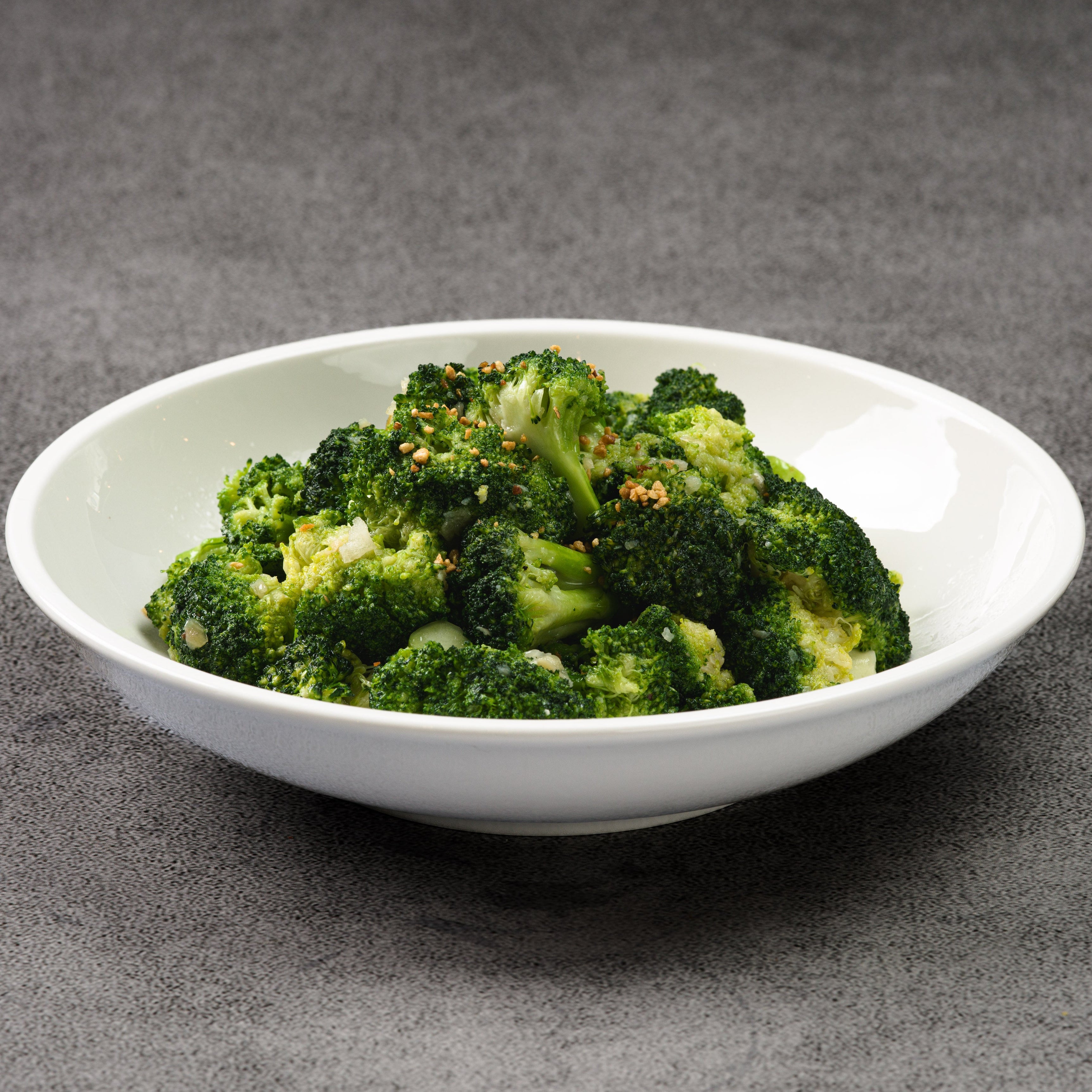 White bowl filled with green broccoli on a gray background