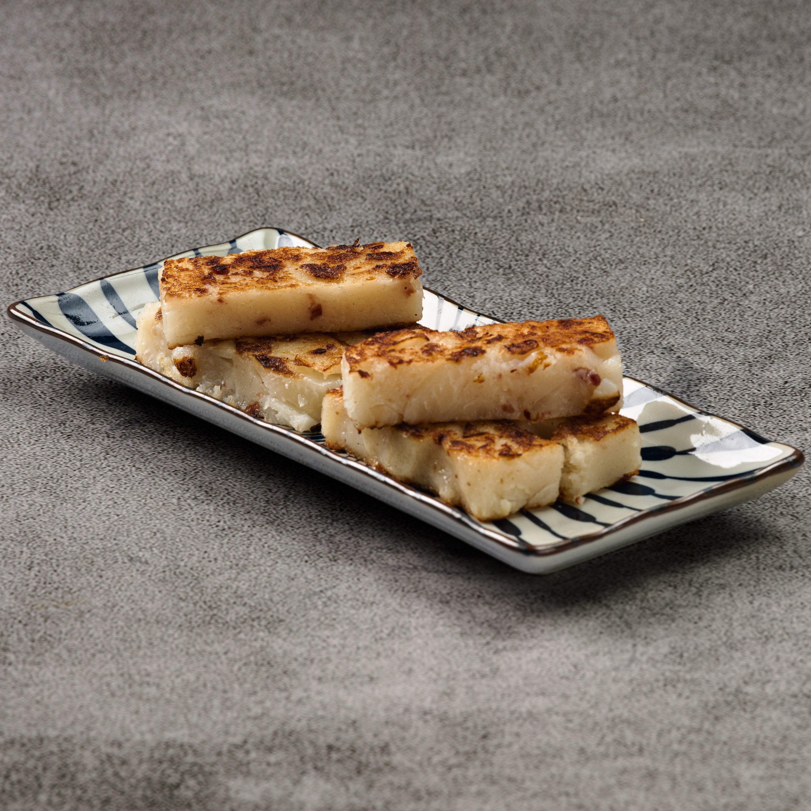 Slices of turnip cake on a decorative plate with a gray background