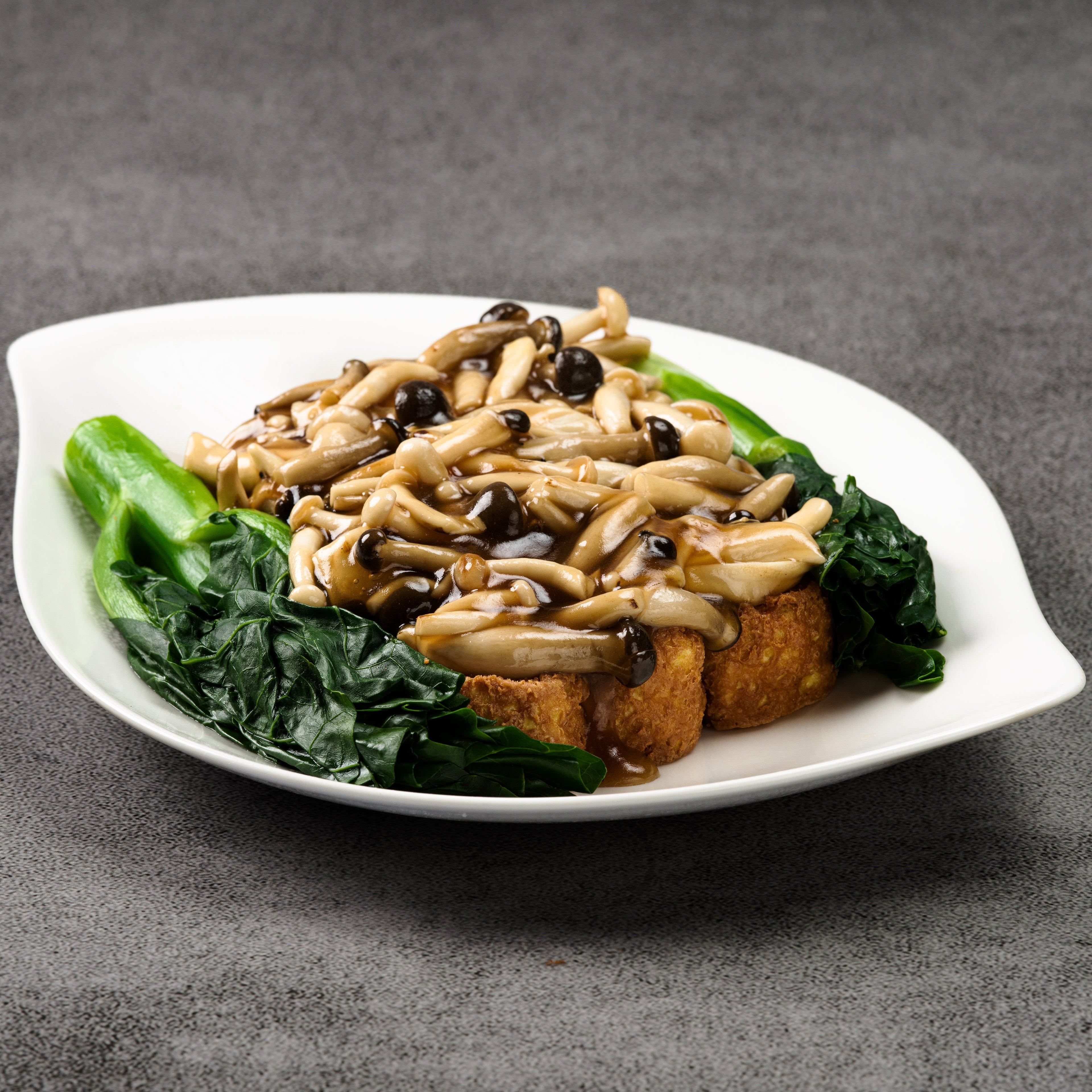 Plated dish with mushrooms on fried tofu and greens on a gray background