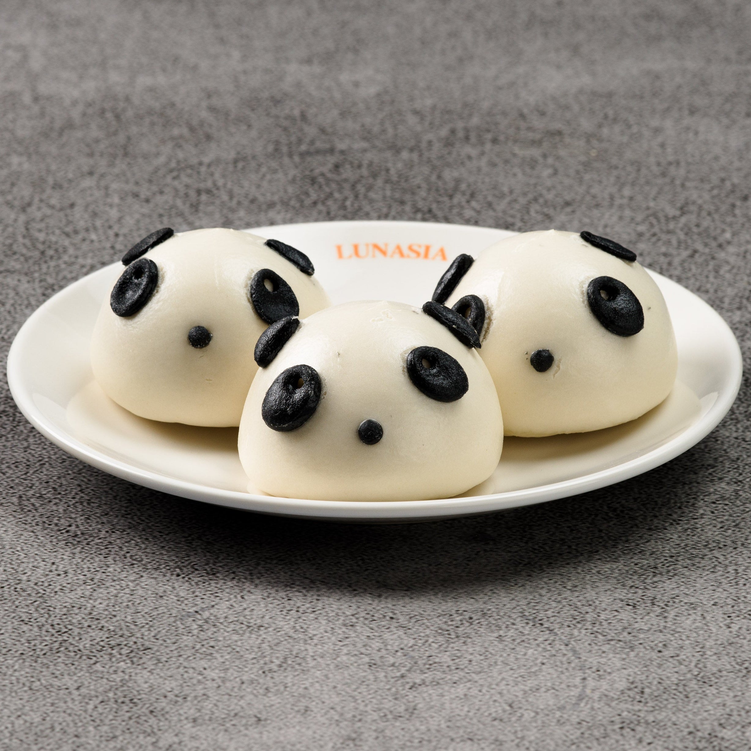 Three panda-shaped buns on a white plate with a gray background