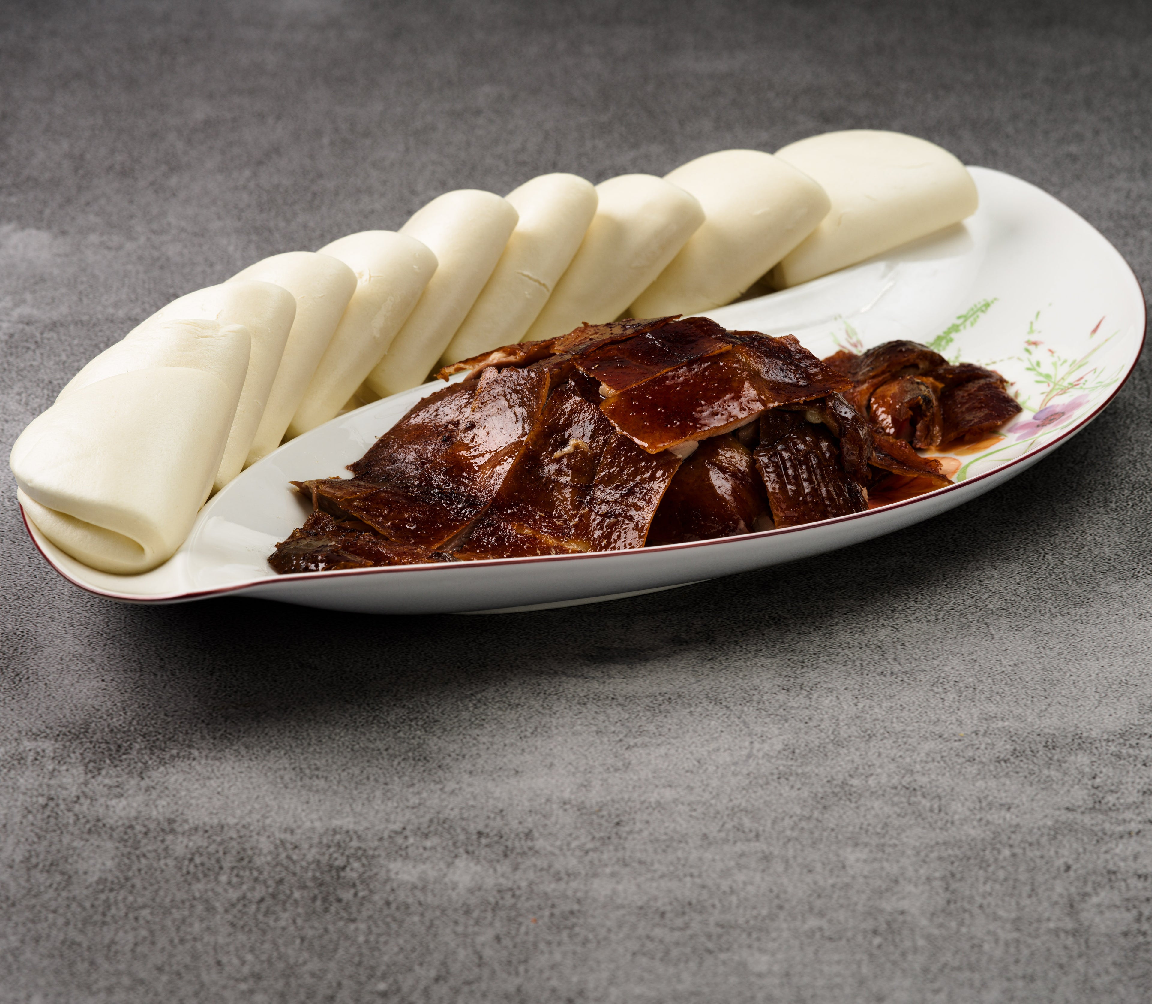 Platter with sliced duck and buns on a gray surface