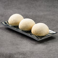 Three white spherical rice puffs on a black rectangular plate against a gray background
