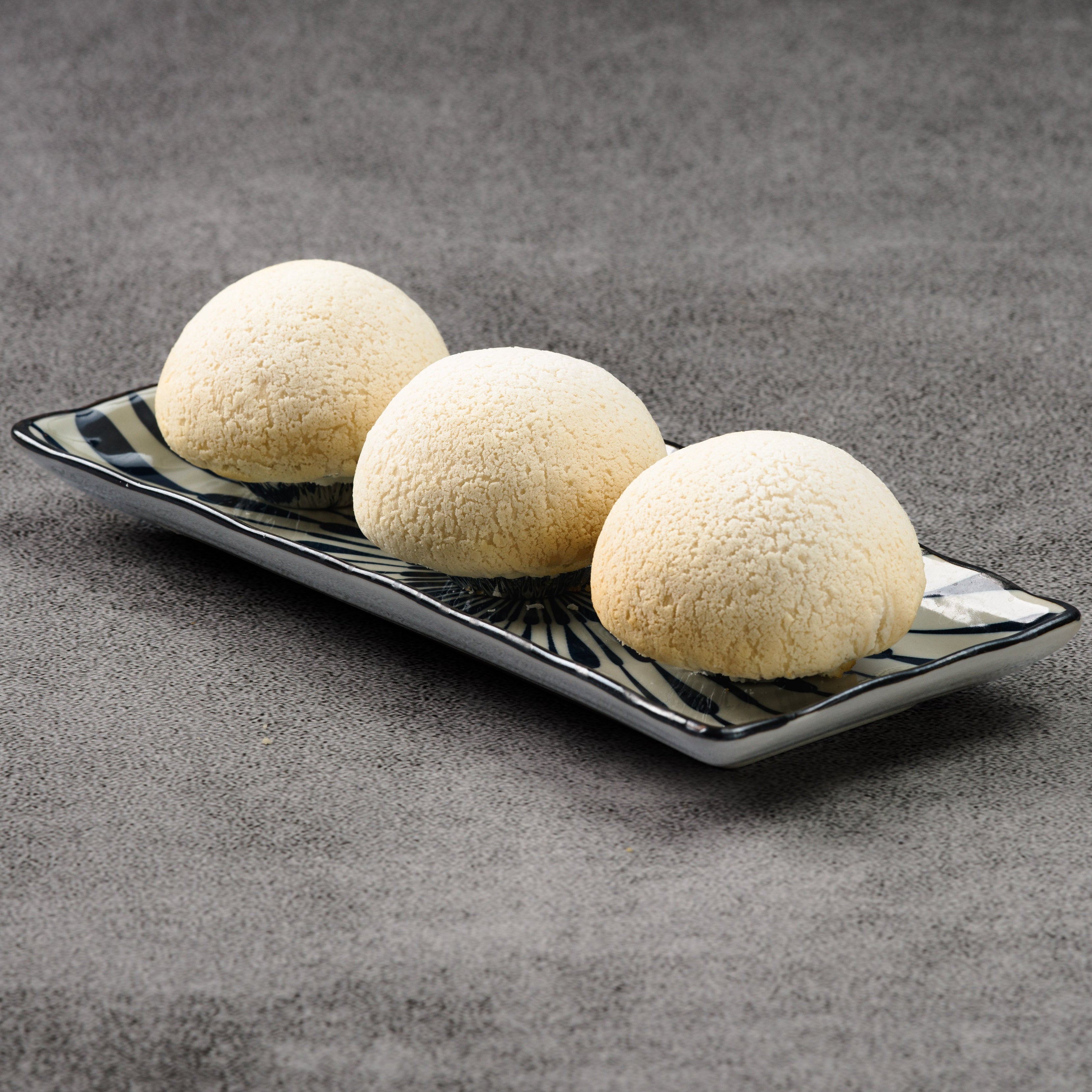 Three white spherical rice puffs on a black rectangular plate against a gray background