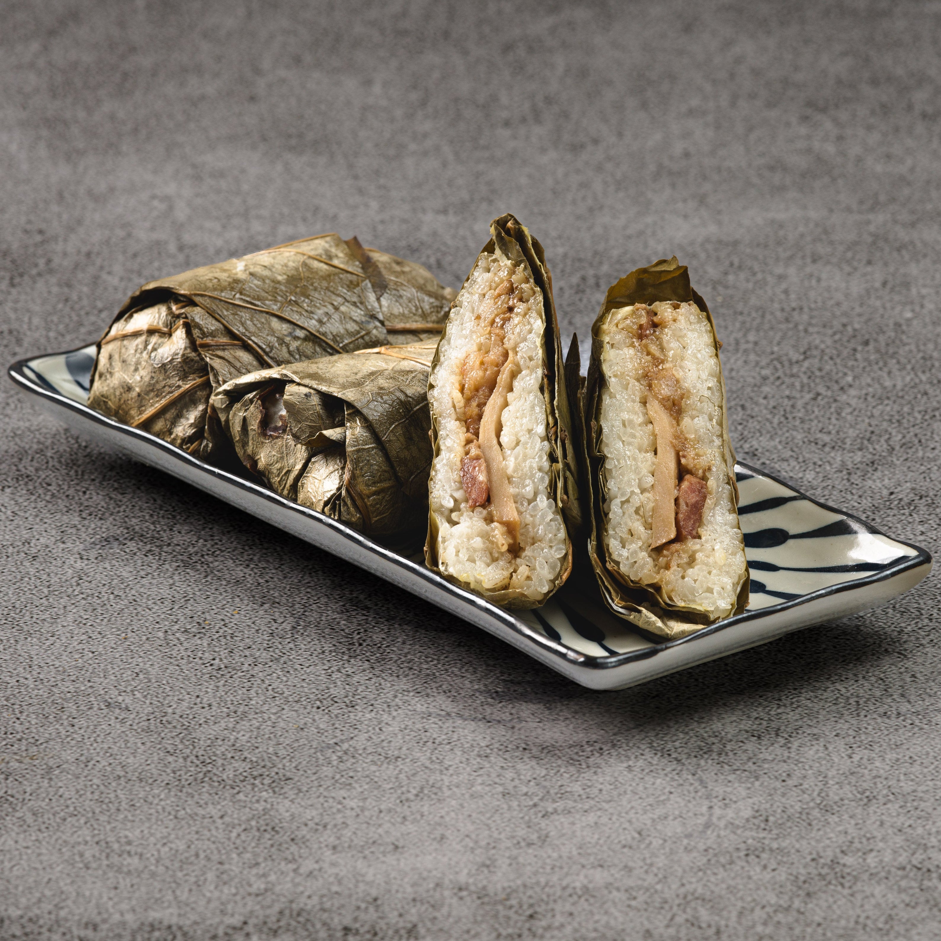Three sticky rice wraps on a rectangular plate with a gray background