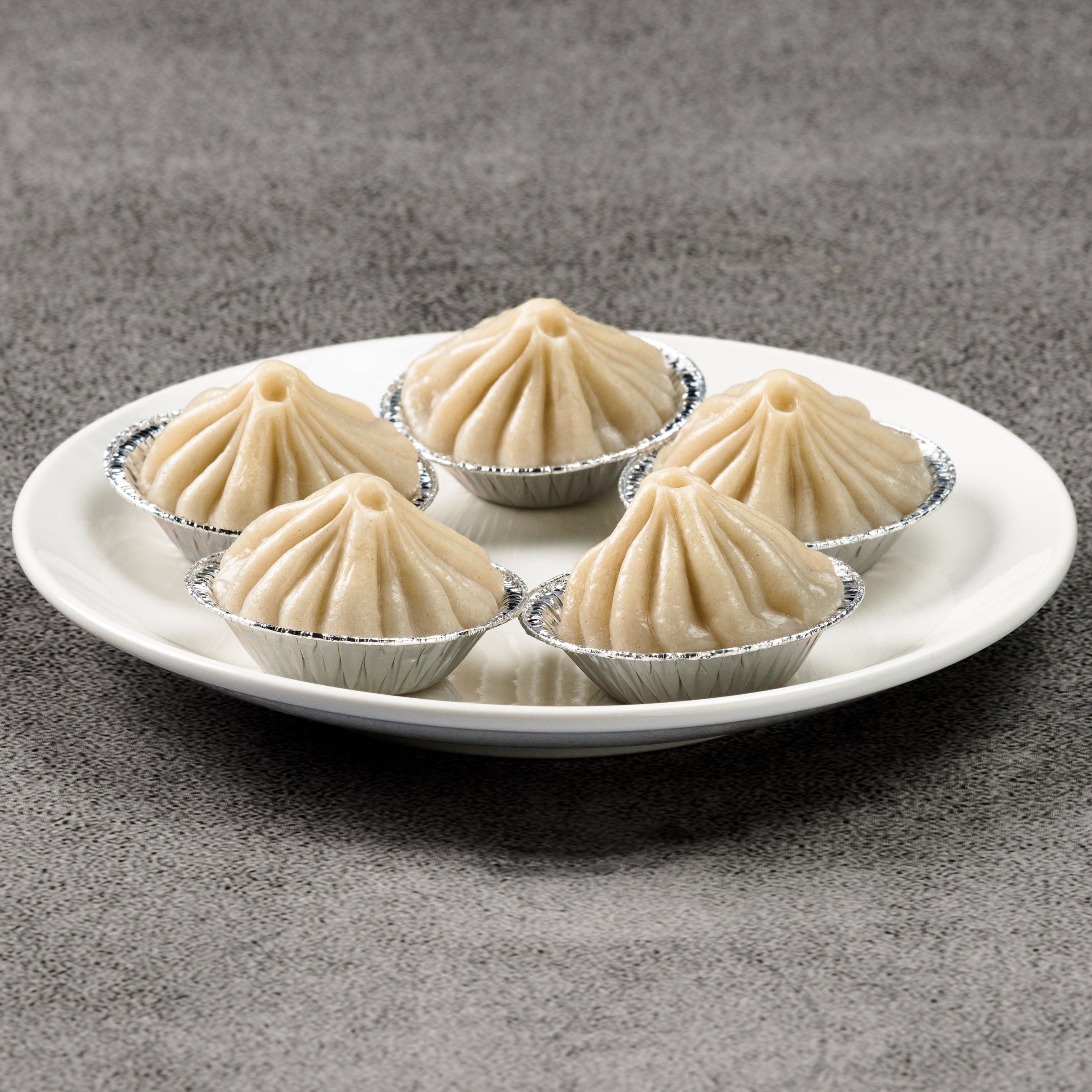 Five soup dumplings on a white plate against a gray background