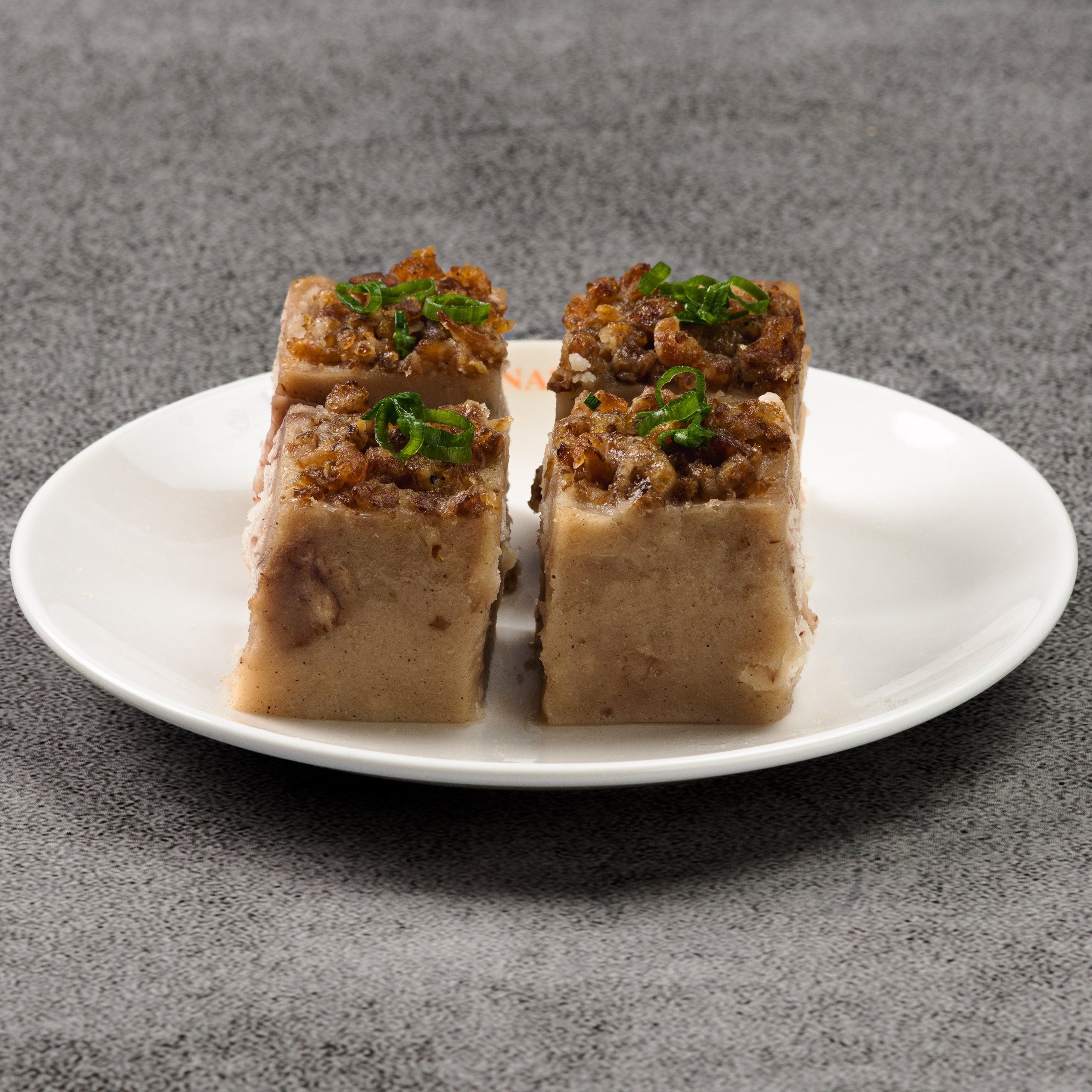 Four pieces of sausage taro cake with garnishes on a white plate against a gray background