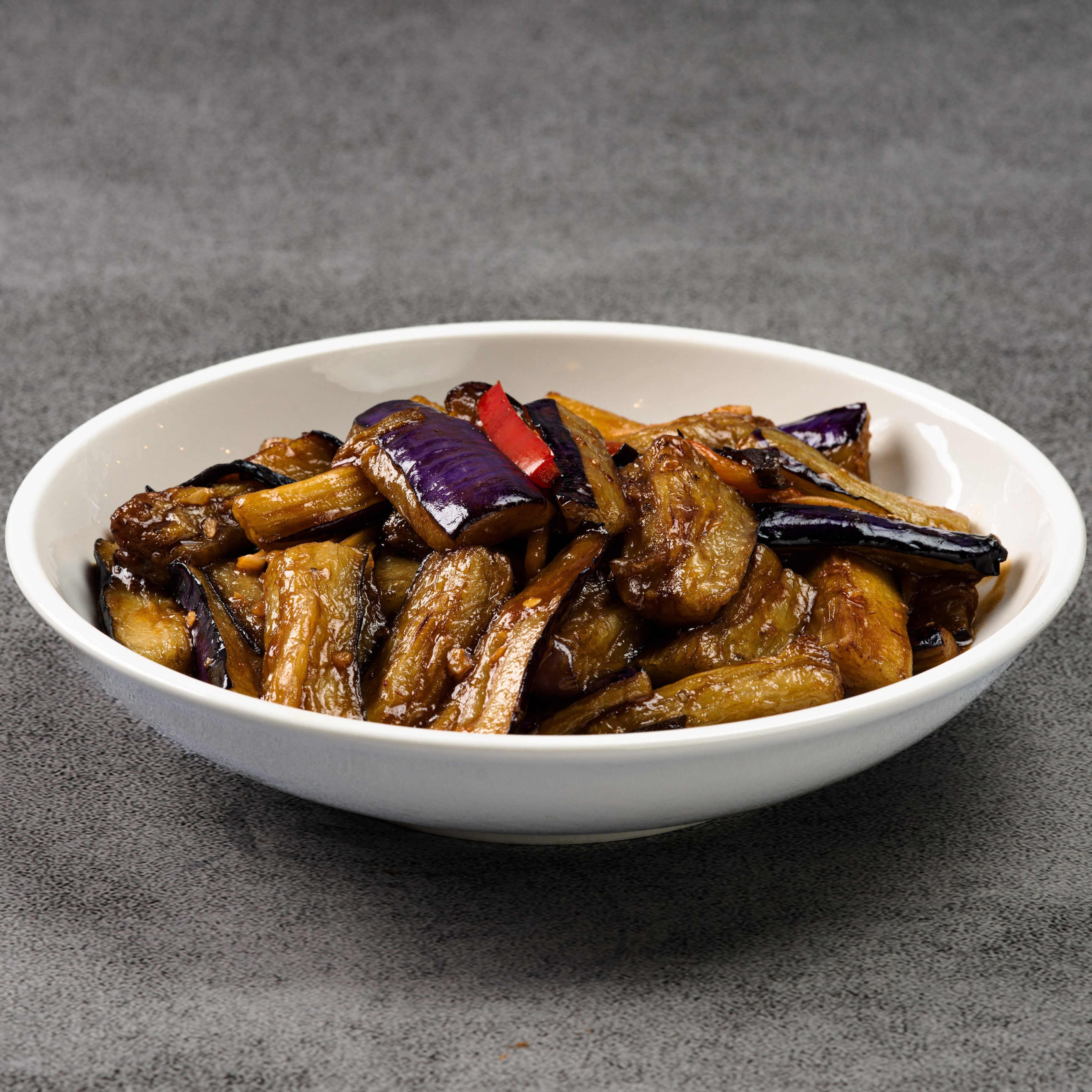 White bowl filled with cooked eggplant on a gray background