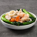 White bowl with seafood and greens on a gray background
