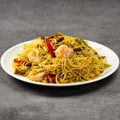 Plate of noodles with shrimp and vegetables on a gray background