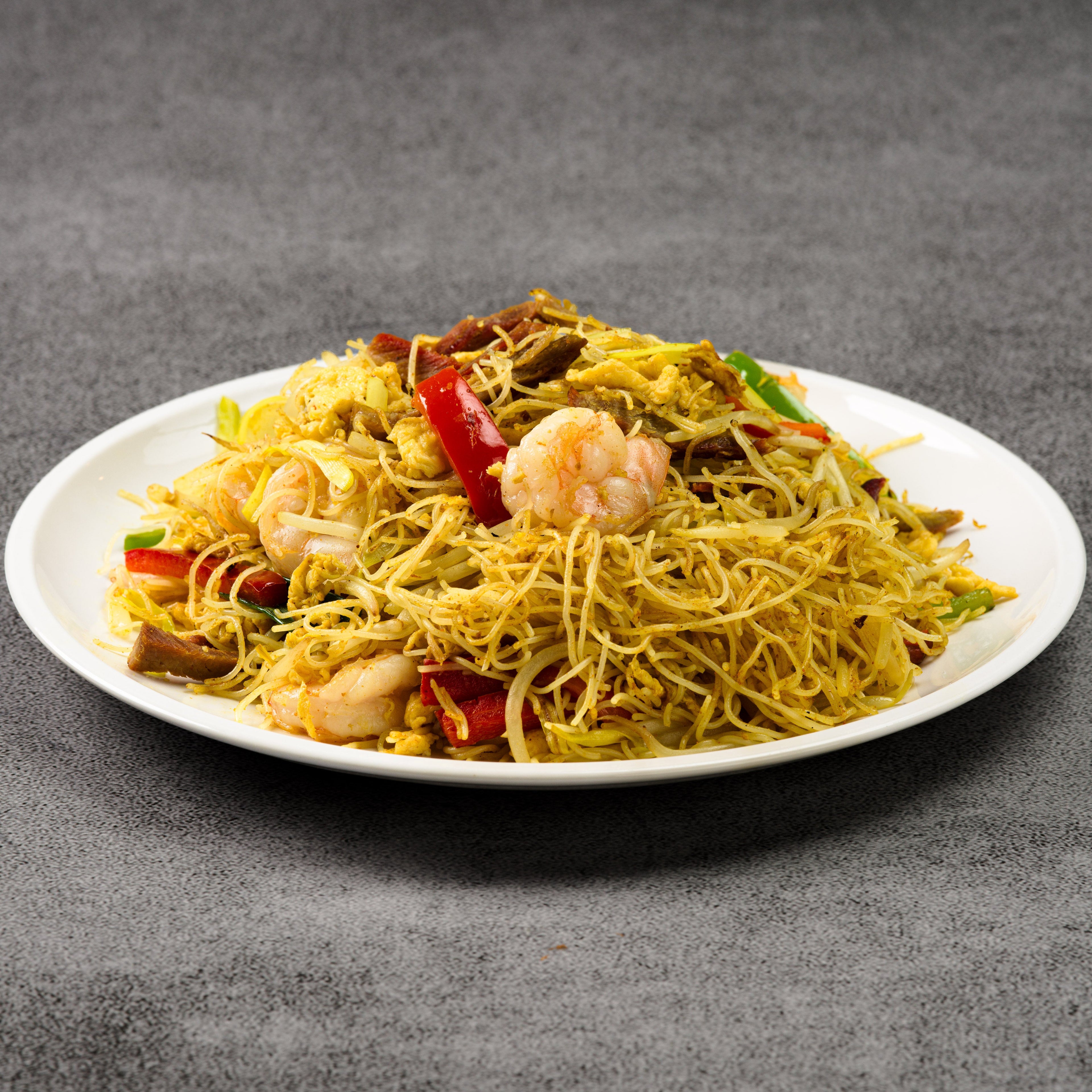 Plate of noodles with shrimp and vegetables on a gray background