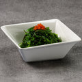 White square bowl with seaweed salad and orange toppings on a gray background