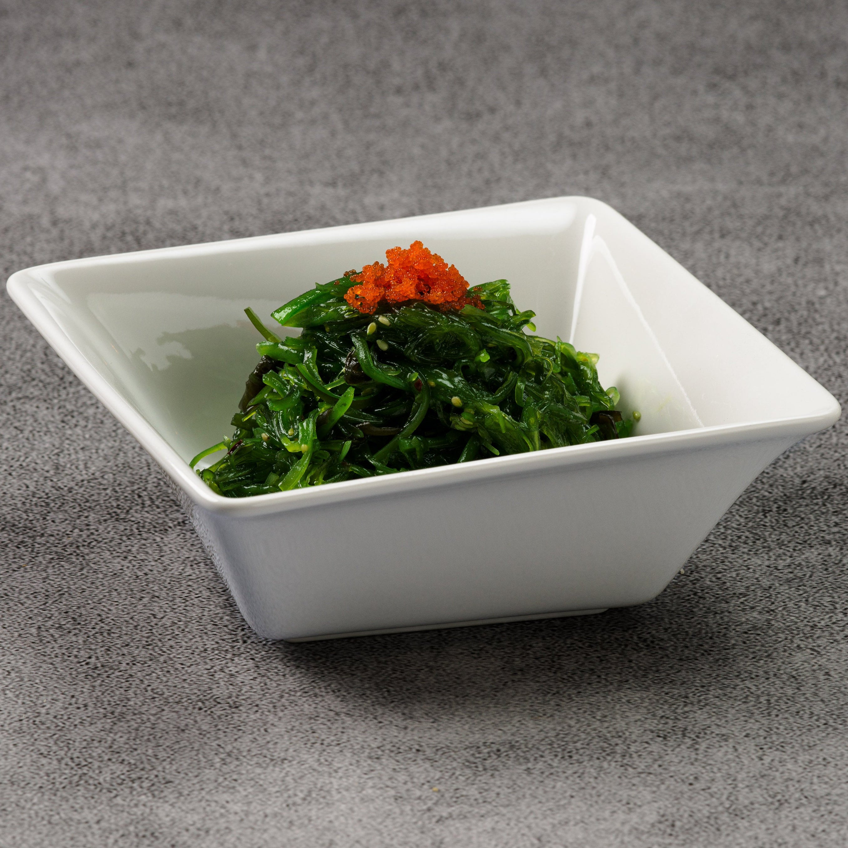 White square bowl with seaweed salad and orange toppings on a gray background