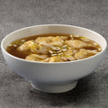 White bowl of soup with wontons on a gray background