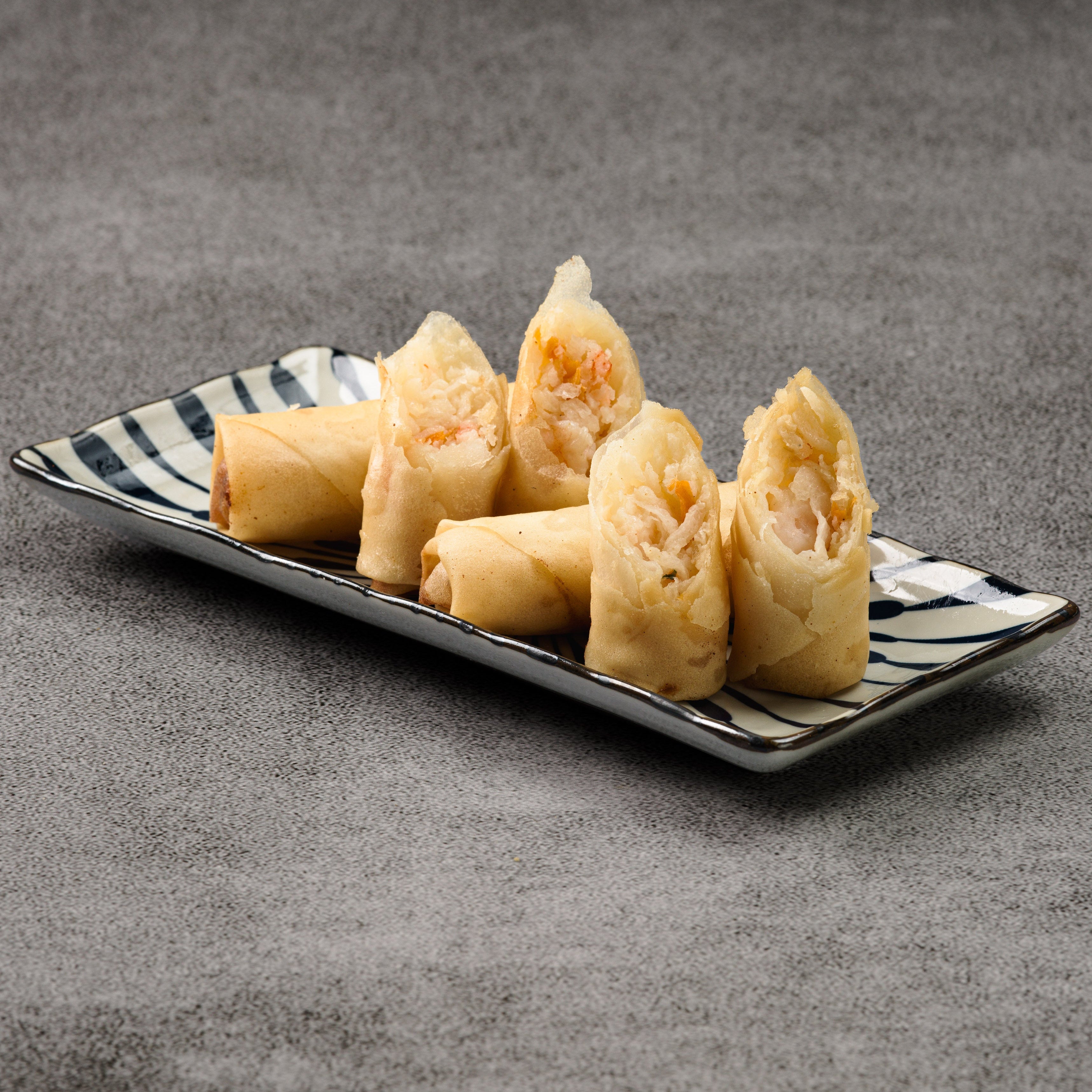 Shrimp rolls on a black and white striped plate against a gray background